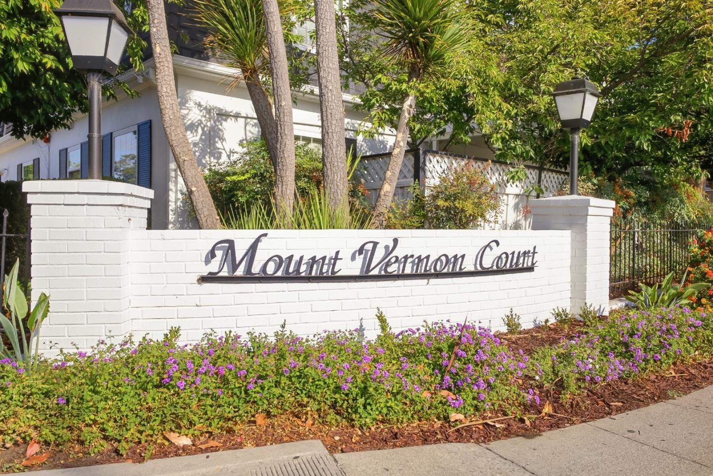 Mount Vernon Court entrance sign on a white brick wall amid flowers and trees.