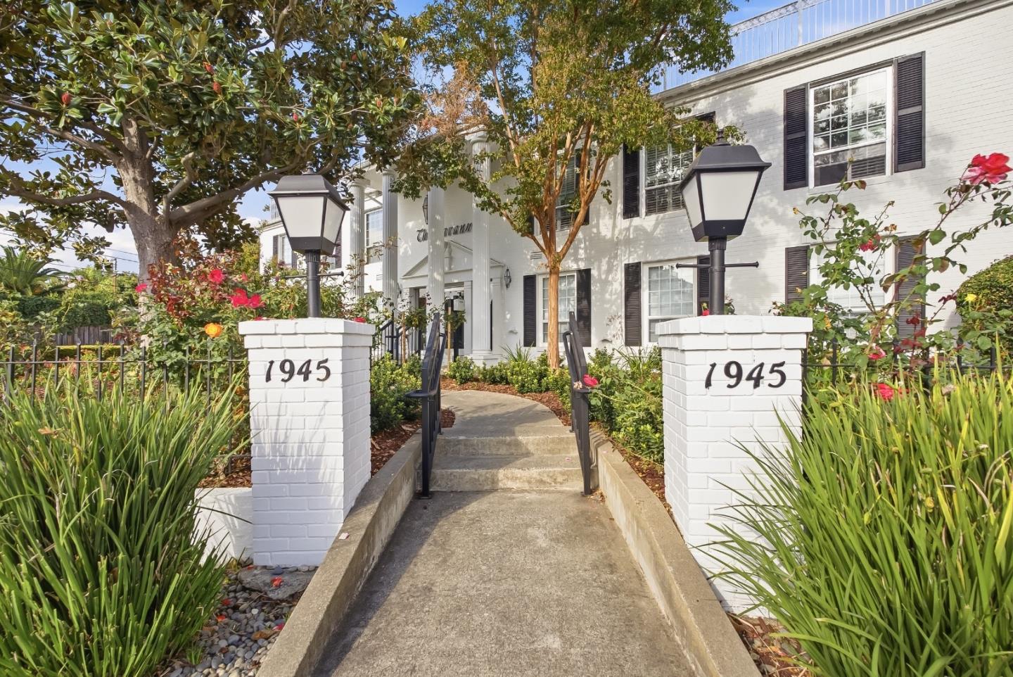 White two-story residence with black shutters and a landscaped walkway flanked by pillars marked 1945.