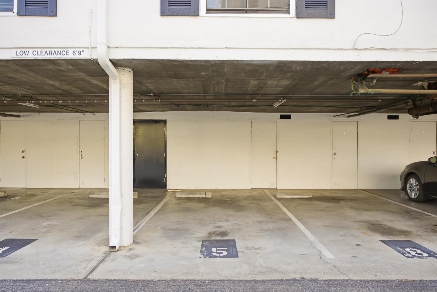 Covered parking area with marked spaces, a low-clearance sign, and a car at the edge.