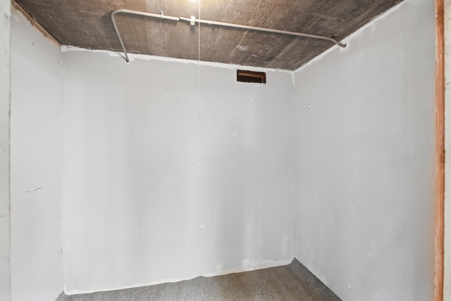 Unfinished basement room with exposed concrete ceiling, overhead pipes, and carpeted floor.