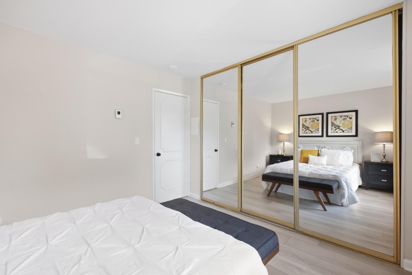 Staged bedroom with mirrored closet doors reflecting a bed, nightstands, and framed artwork.