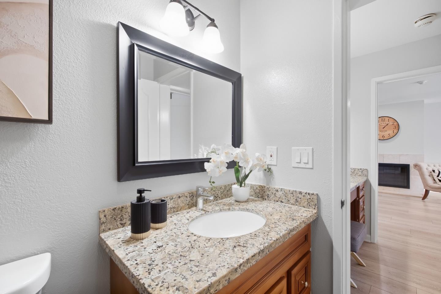 Bathroom vanity with a granite counter, wood cabinetry, and a black-framed mirror.