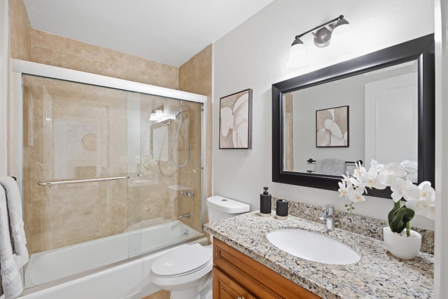 Bathroom with a beige stone-tile shower, granite vanity countertop, and large dark-framed mirror.