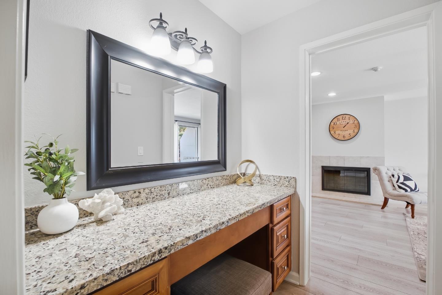 Bathroom vanity with a granite counter and large mirror, opening to a sitting area with a fireplace.