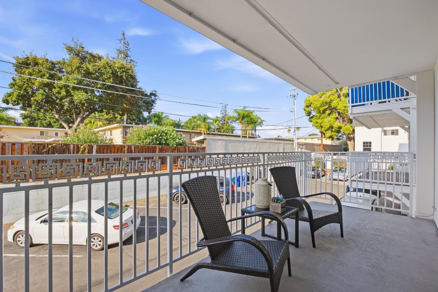 Covered balcony with two wicker chairs and a view of the parking area.