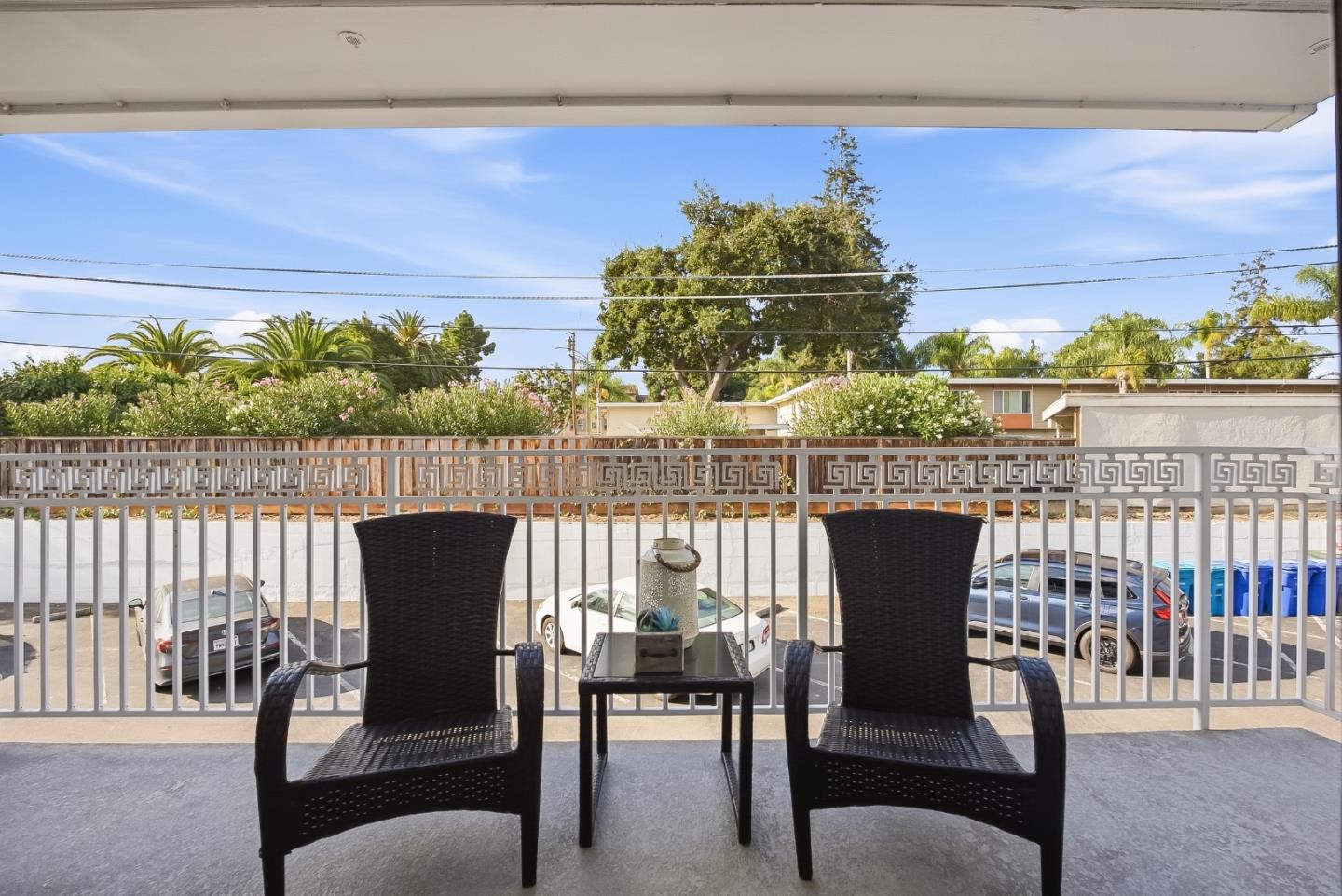 Covered balcony with wicker seating overlooking parked cars and neighboring homes.