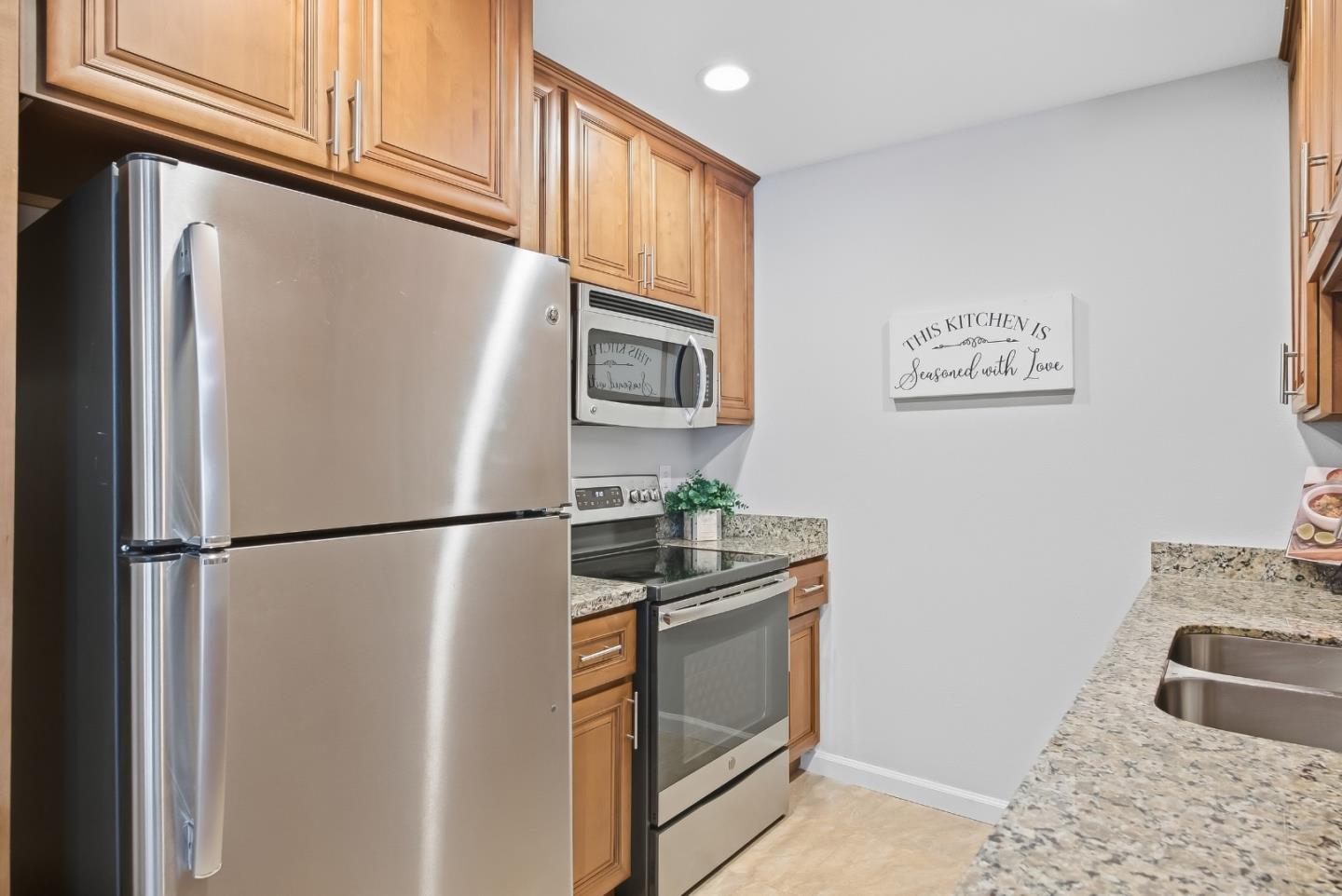Kitchen with honey-toned wood cabinets, stainless steel appliances, granite counters, and a wall sign.