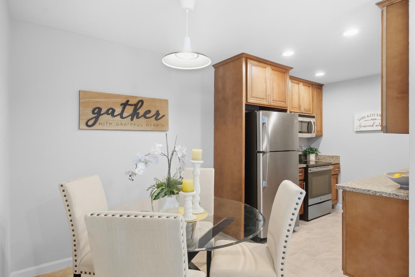Dining area beside a kitchen with wood cabinets, stainless steel appliances, and a glass table.