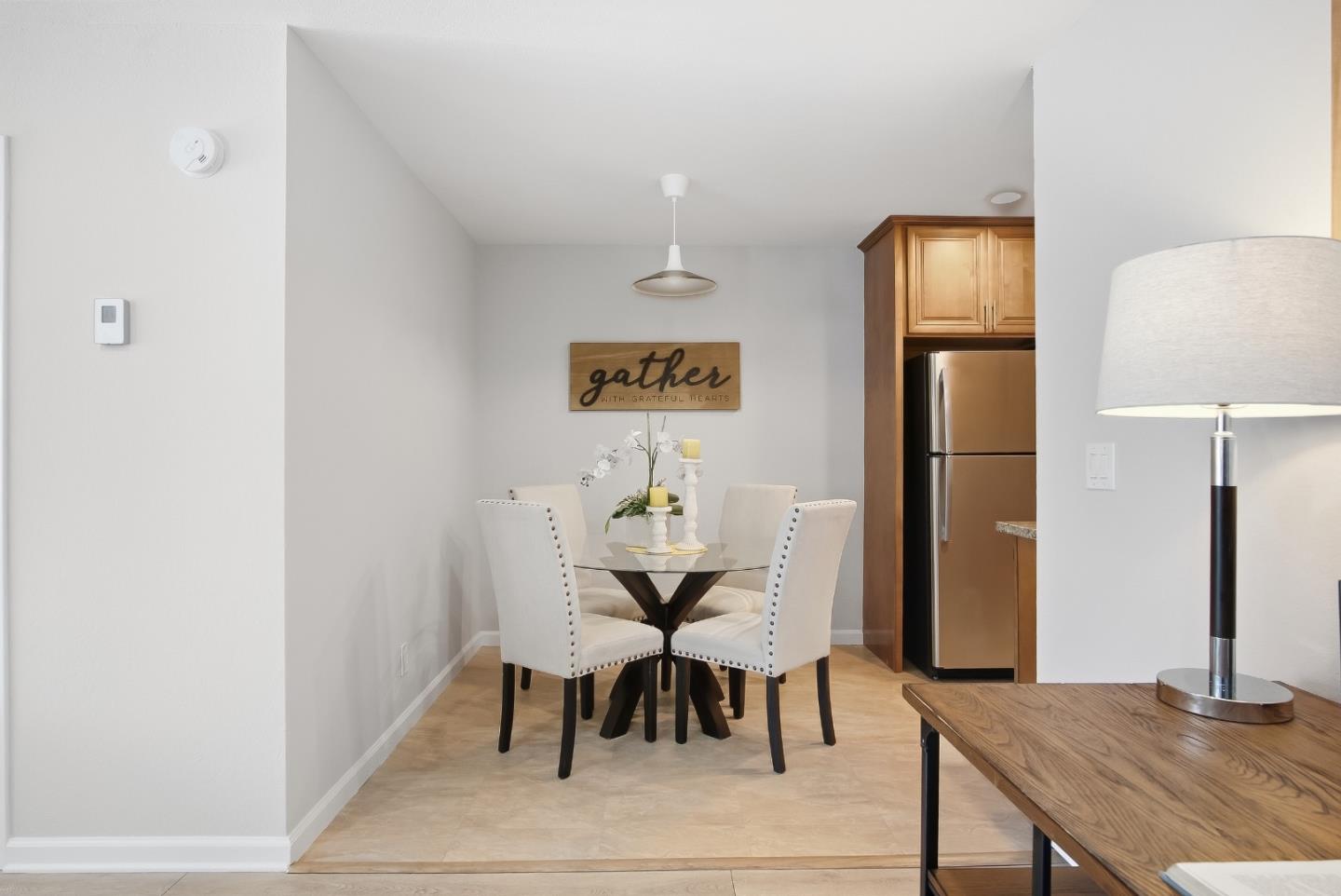 Dining nook with a glass-top table, cream chairs, and wood cabinetry beside a stainless steel refrigerator.
