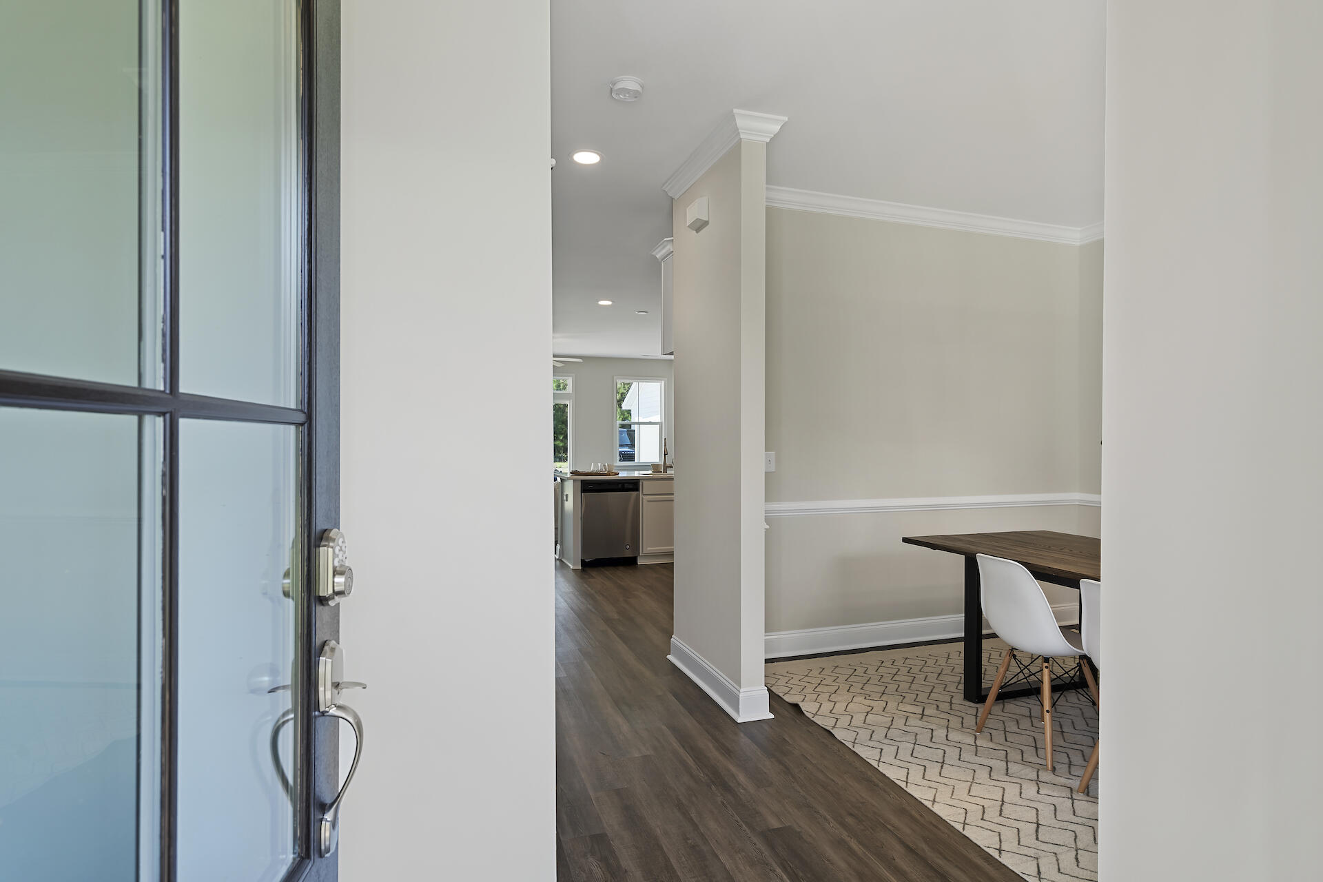Open front door reveals a dining area with a dark table and a kitchen beyond.