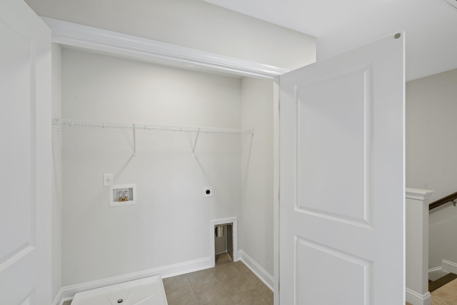 Empty laundry room with wire shelf, washer hookups, tiled floor, and a small pet door.