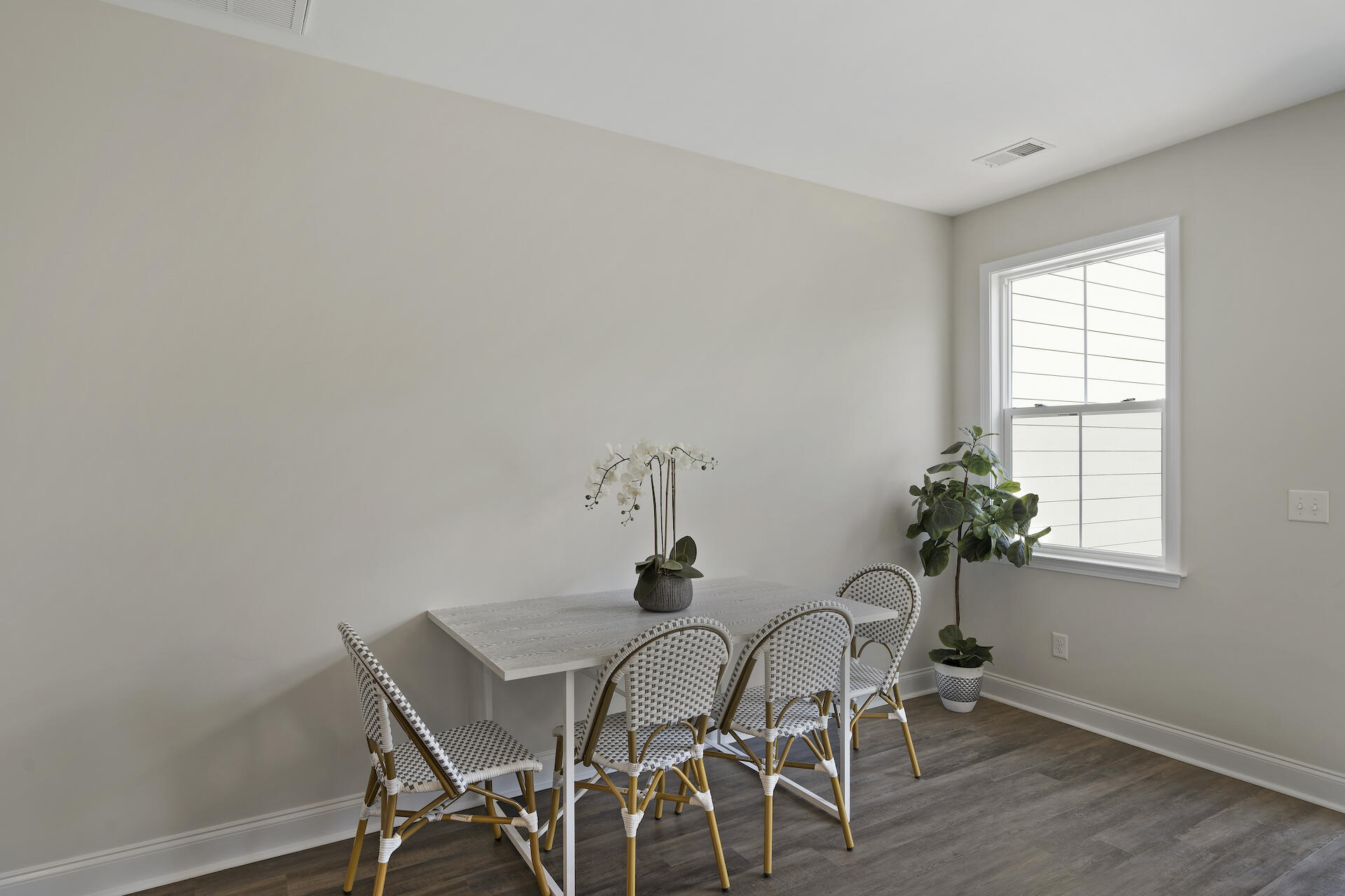 Dining area with a white table, woven chairs, a bright window, and potted plants.