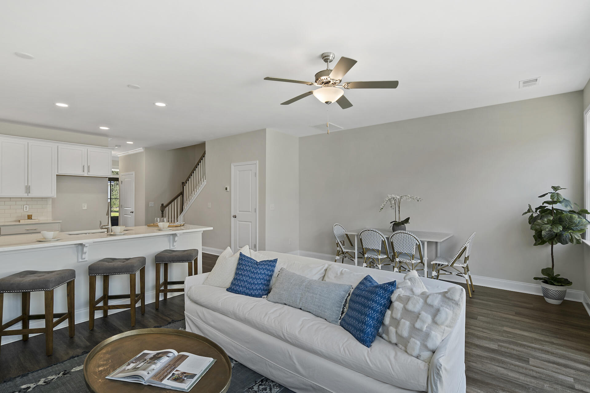 Open-plan living room with a white sofa and blue pillows beside the kitchen island and dining area.