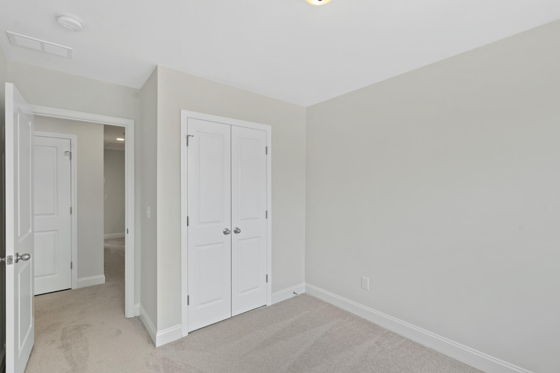 Empty bedroom with beige carpet and a white double-door closet beside the open doorway.