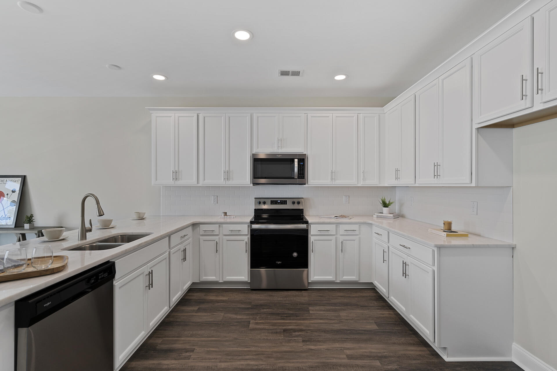 Kitchen with white cabinets, light counters, stainless appliances, and dark wood floors.