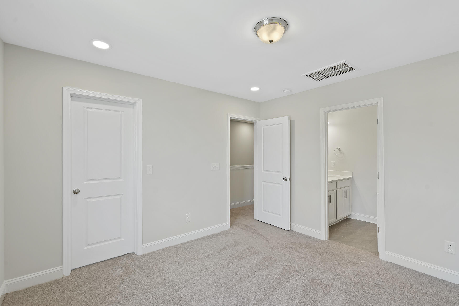 Empty carpeted room with a closet doorway and an adjoining bathroom vanity.