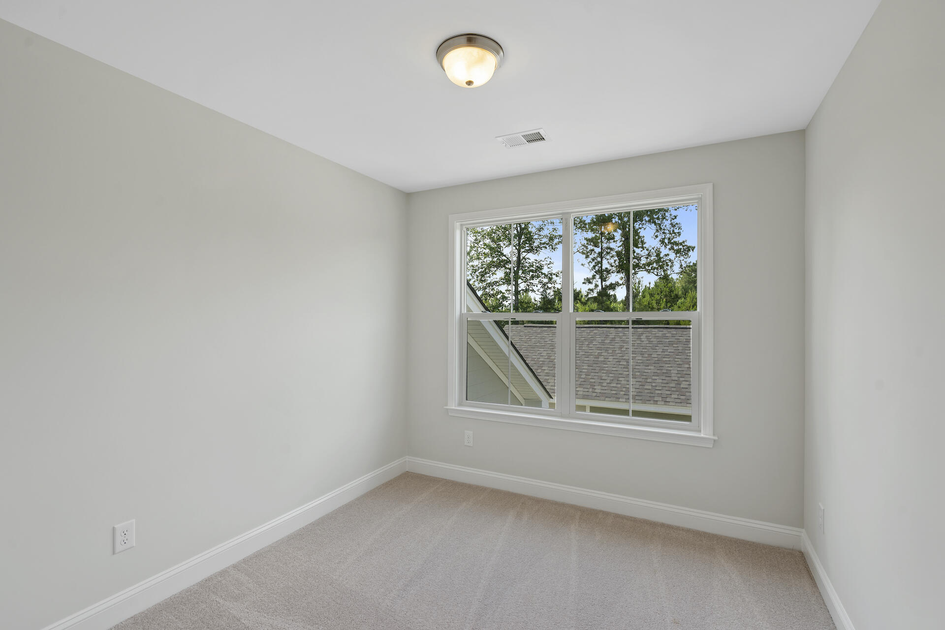 Empty carpeted room with gray walls and a large window overlooking trees.