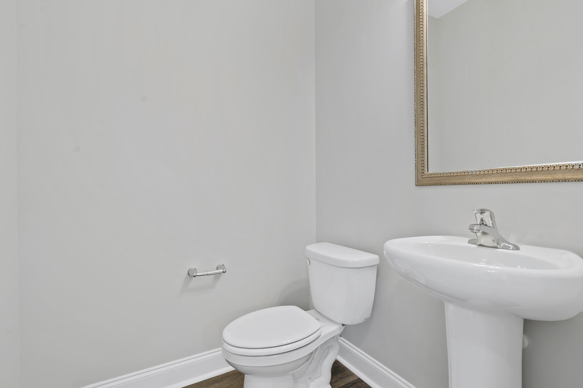 Bathroom with a white toilet, pedestal sink, chrome fixtures, and framed mirror.