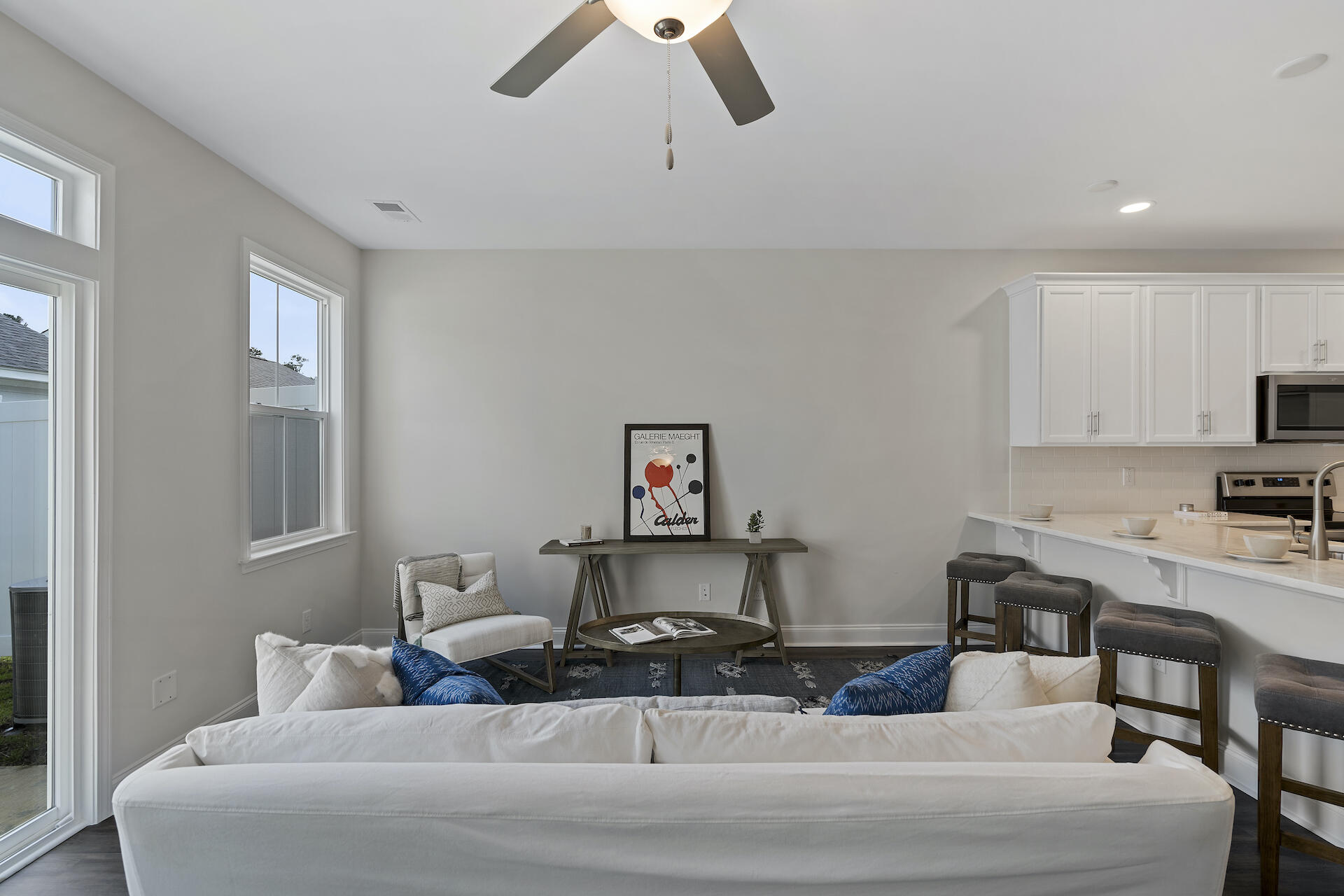 Living room with a white sofa, ceiling fan, and open kitchen with a breakfast bar.