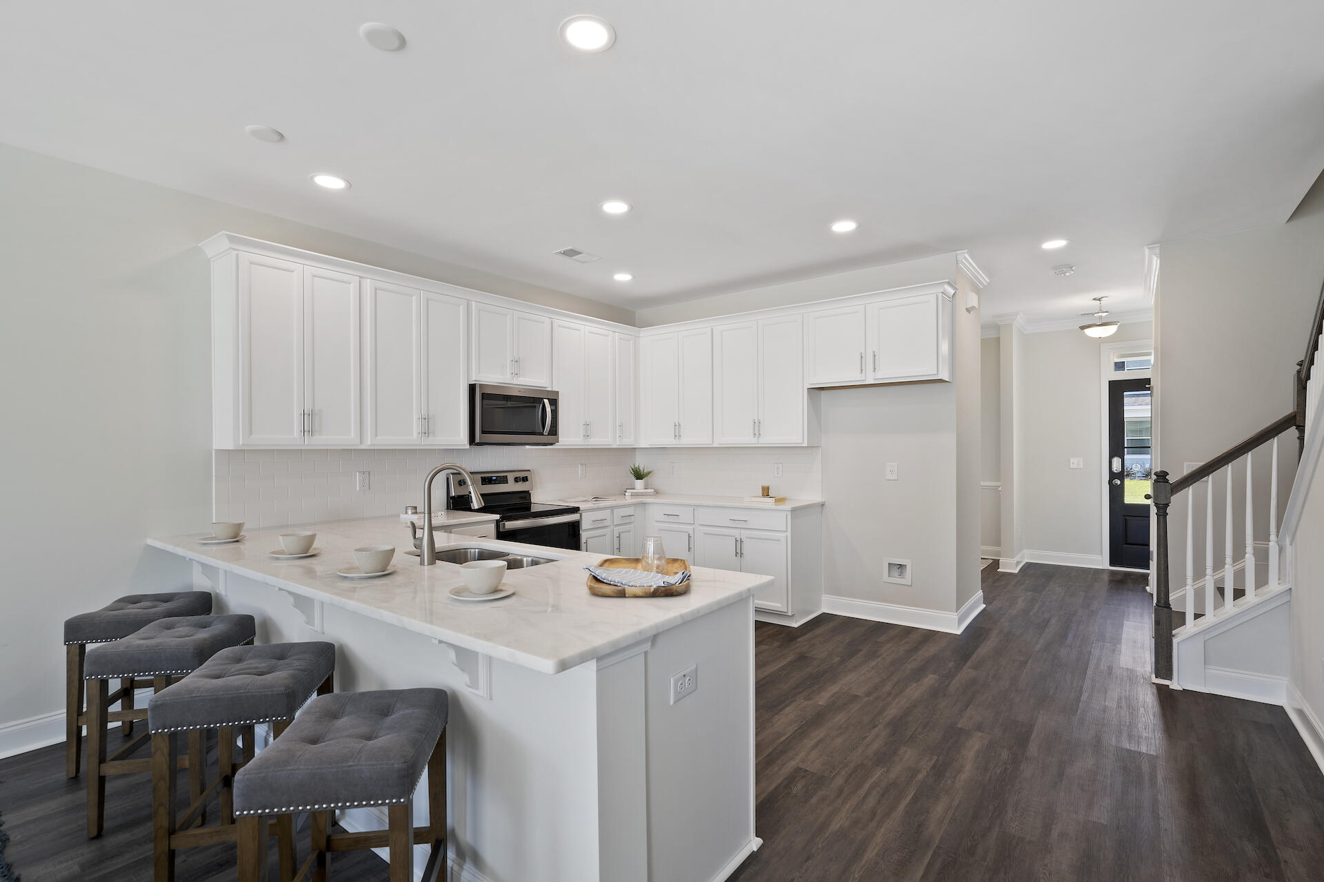 Kitchen with white cabinetry, a large island with breakfast-bar seating, and dark flooring.
