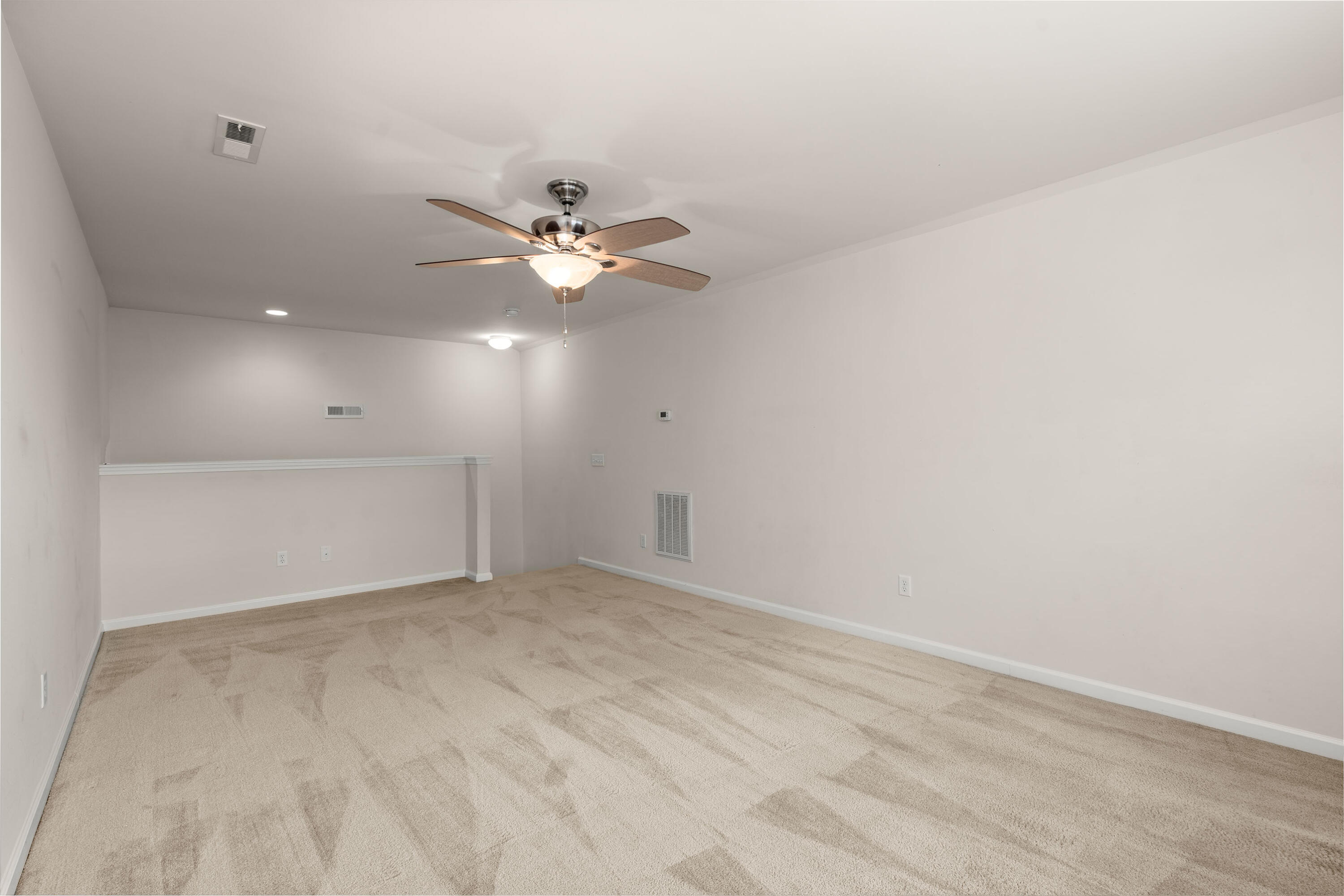 Empty carpeted room with pale walls, a ceiling fan, and a low ledge along the far wall.