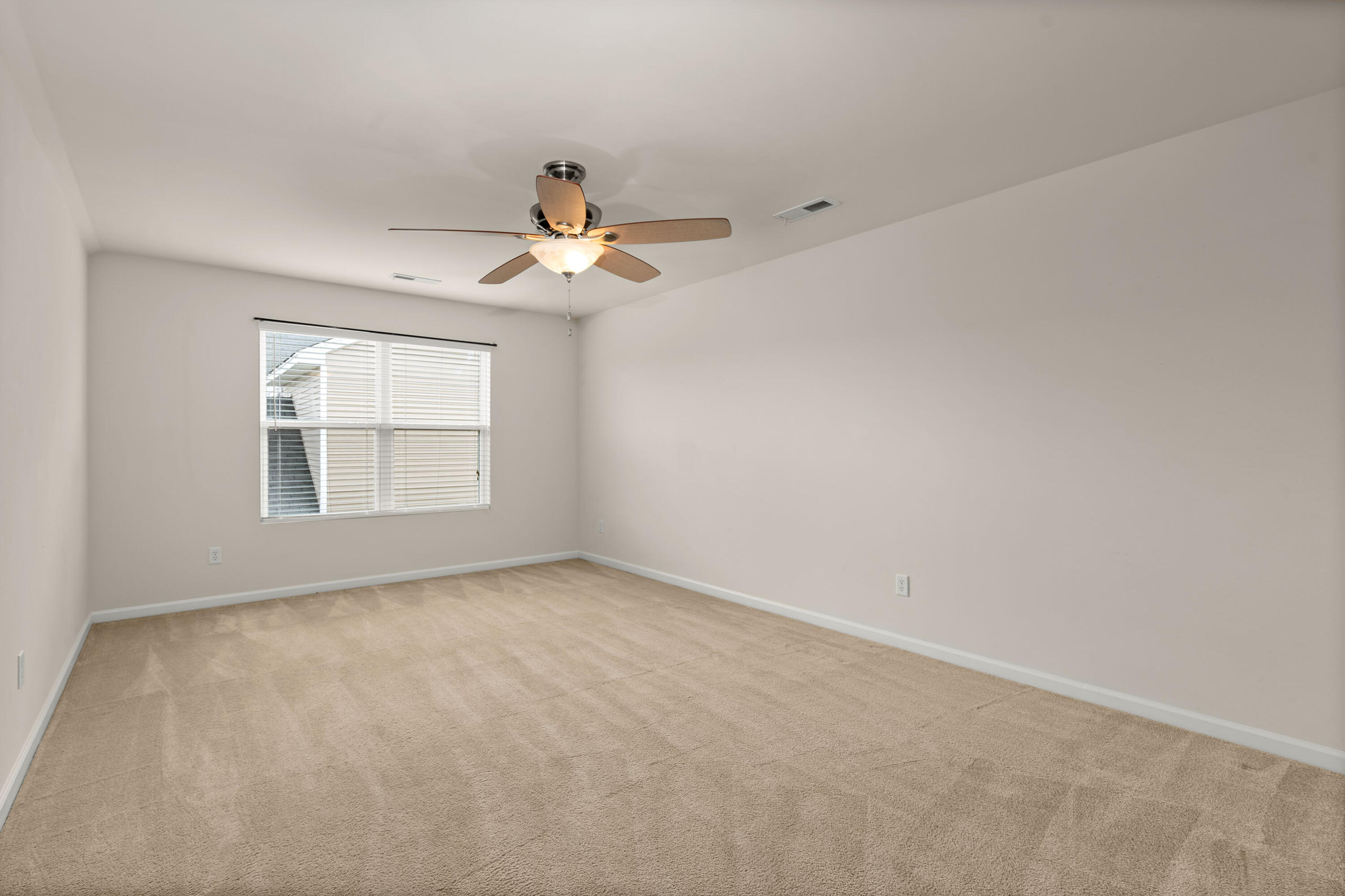 Empty carpeted room with a window and ceiling fan with light.