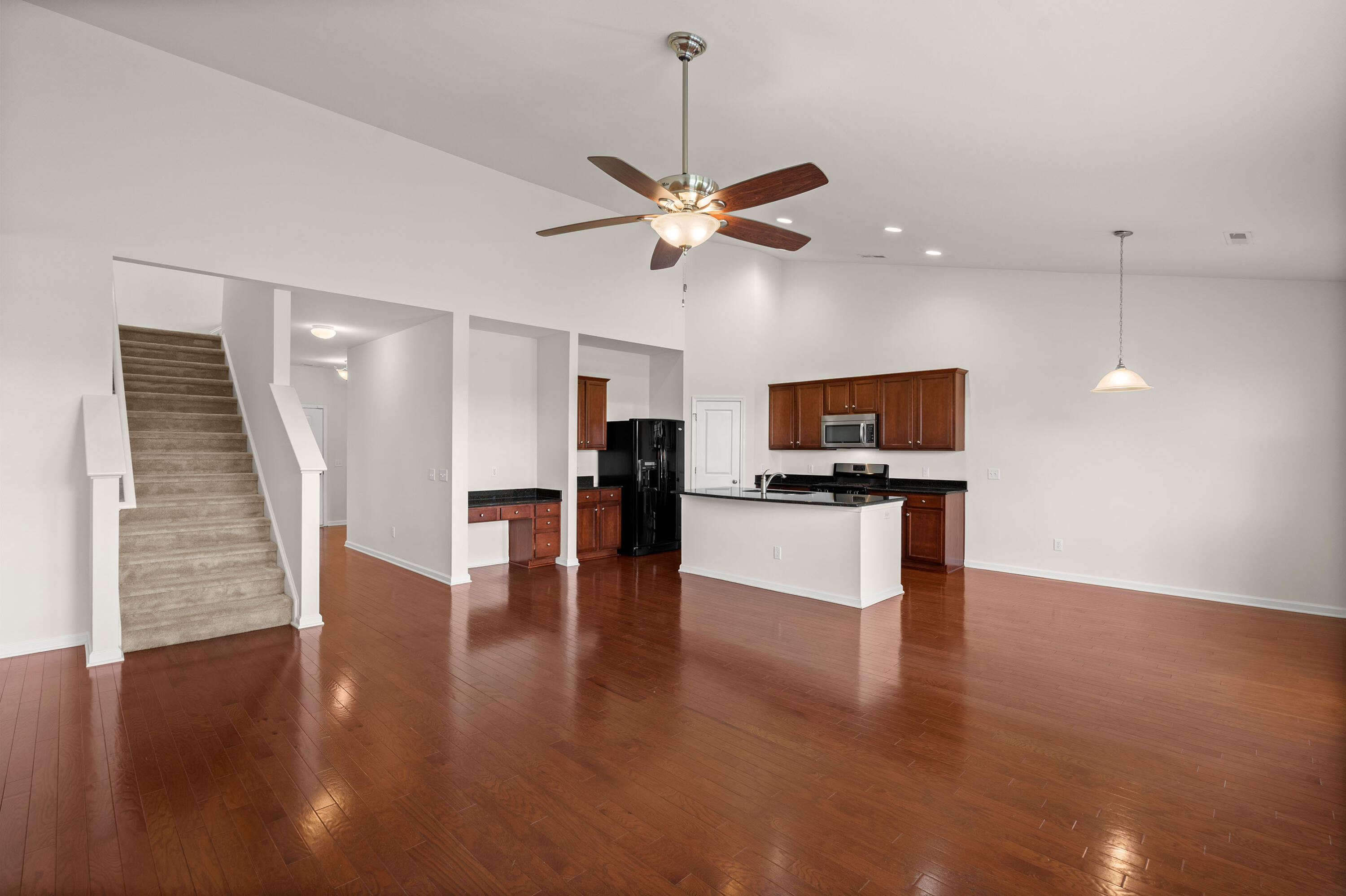 Open kitchen and living area with a white island, dark wood cabinets, hardwood floors, and carpeted stairs.