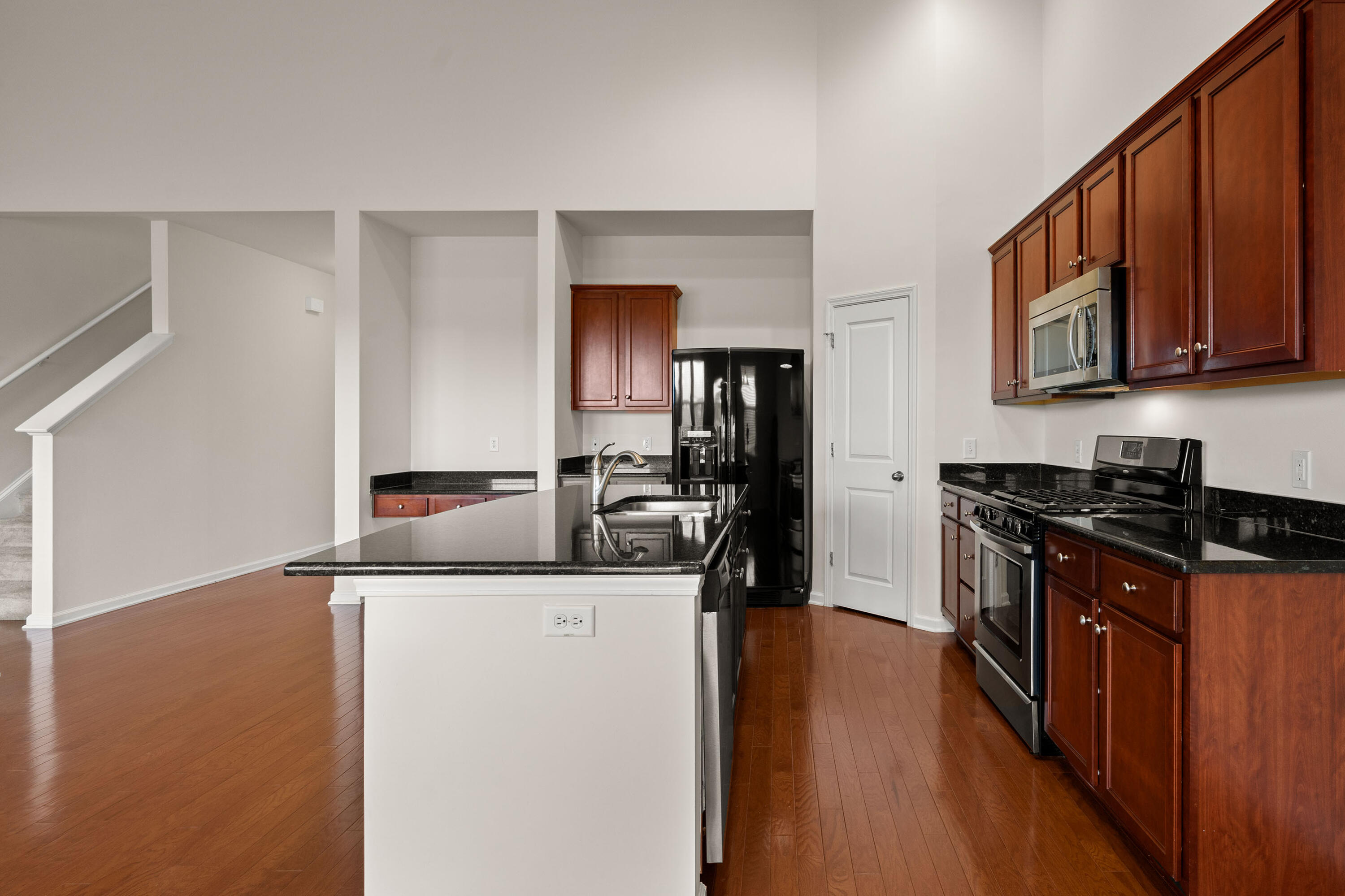 Kitchen with wood cabinets, black granite counters, stainless appliances, and a large island beside an open staircase.