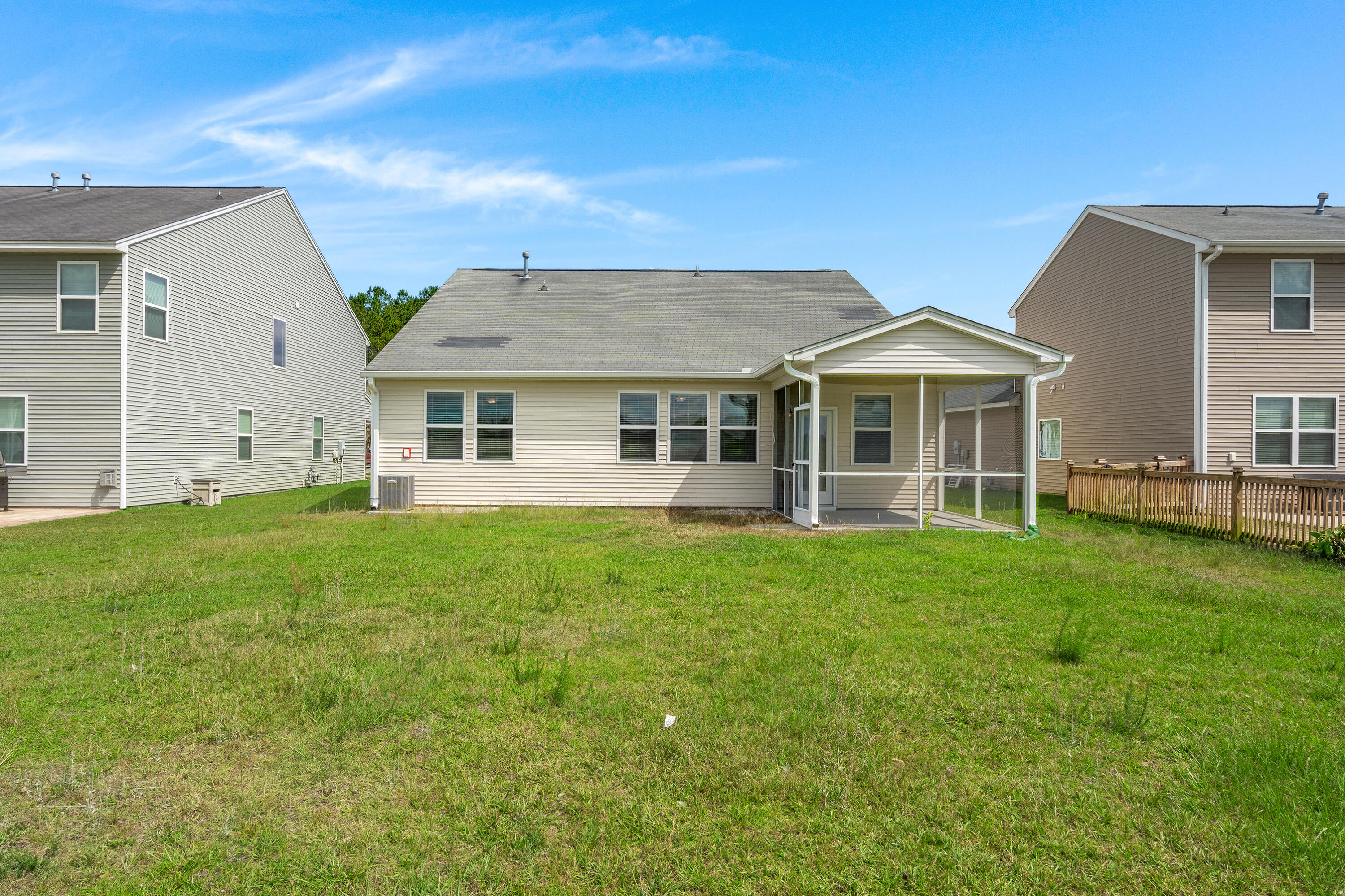 Rear of a beige home with a screened porch and broad grassy backyard.