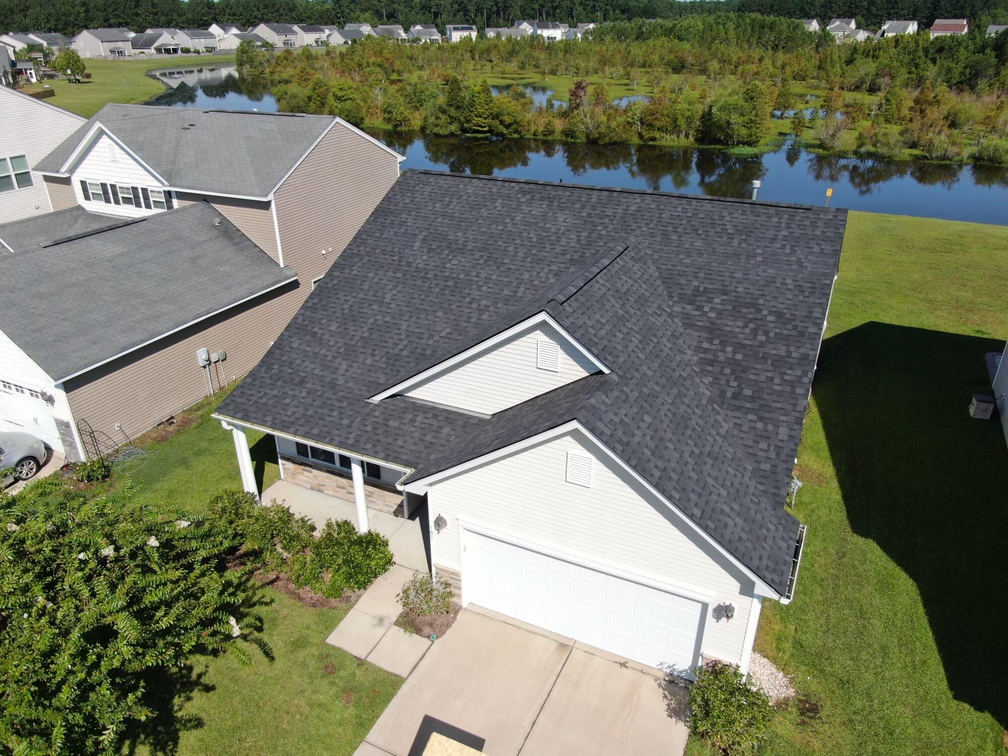Aerial view of a white house with a large dark roof beside a pond.