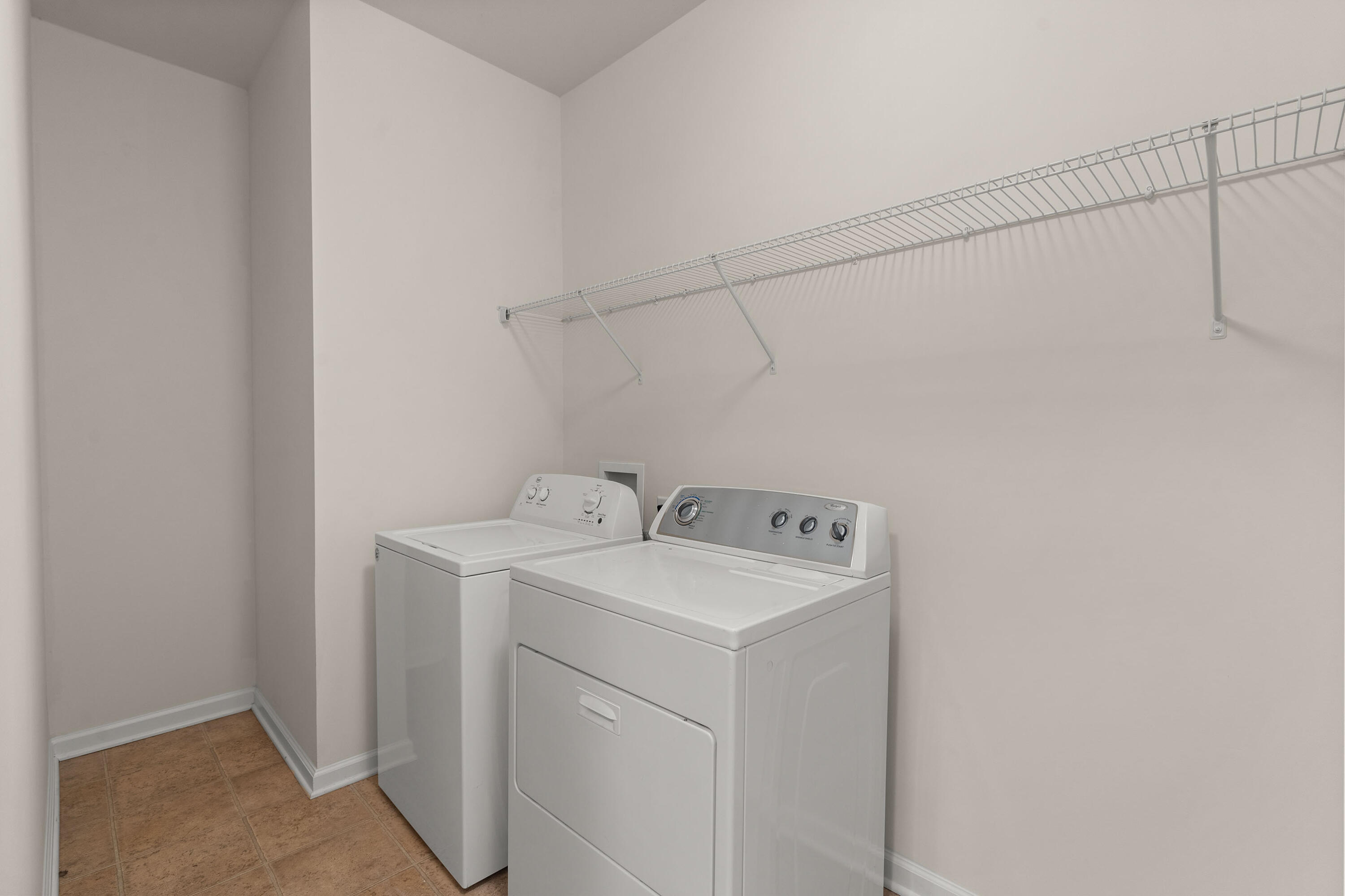 Laundry room with a white washer and dryer beneath a long wire shelf.