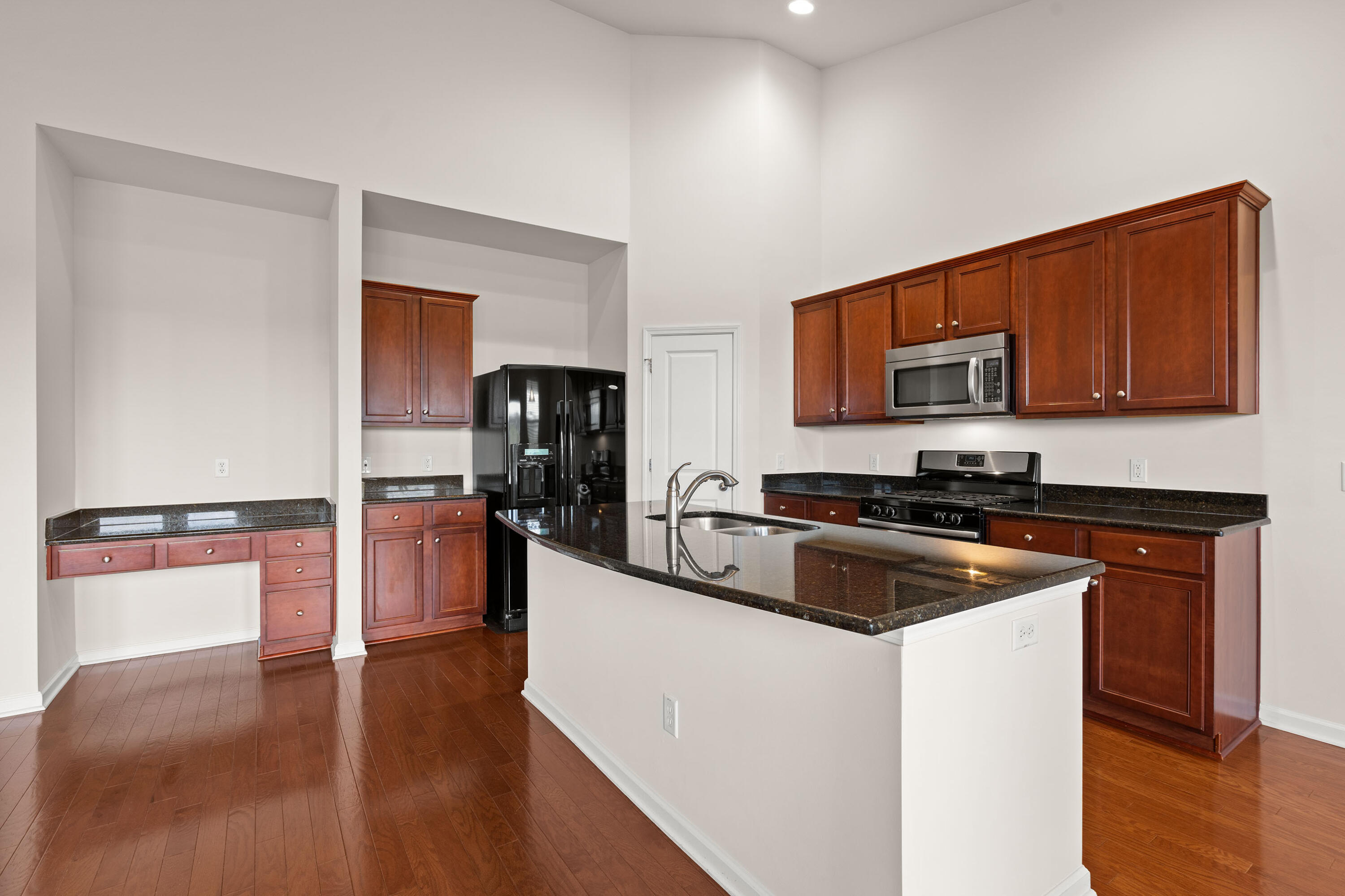 Kitchen with reddish-brown cabinets, dark stone counters, stainless appliances, and a large island with sink.