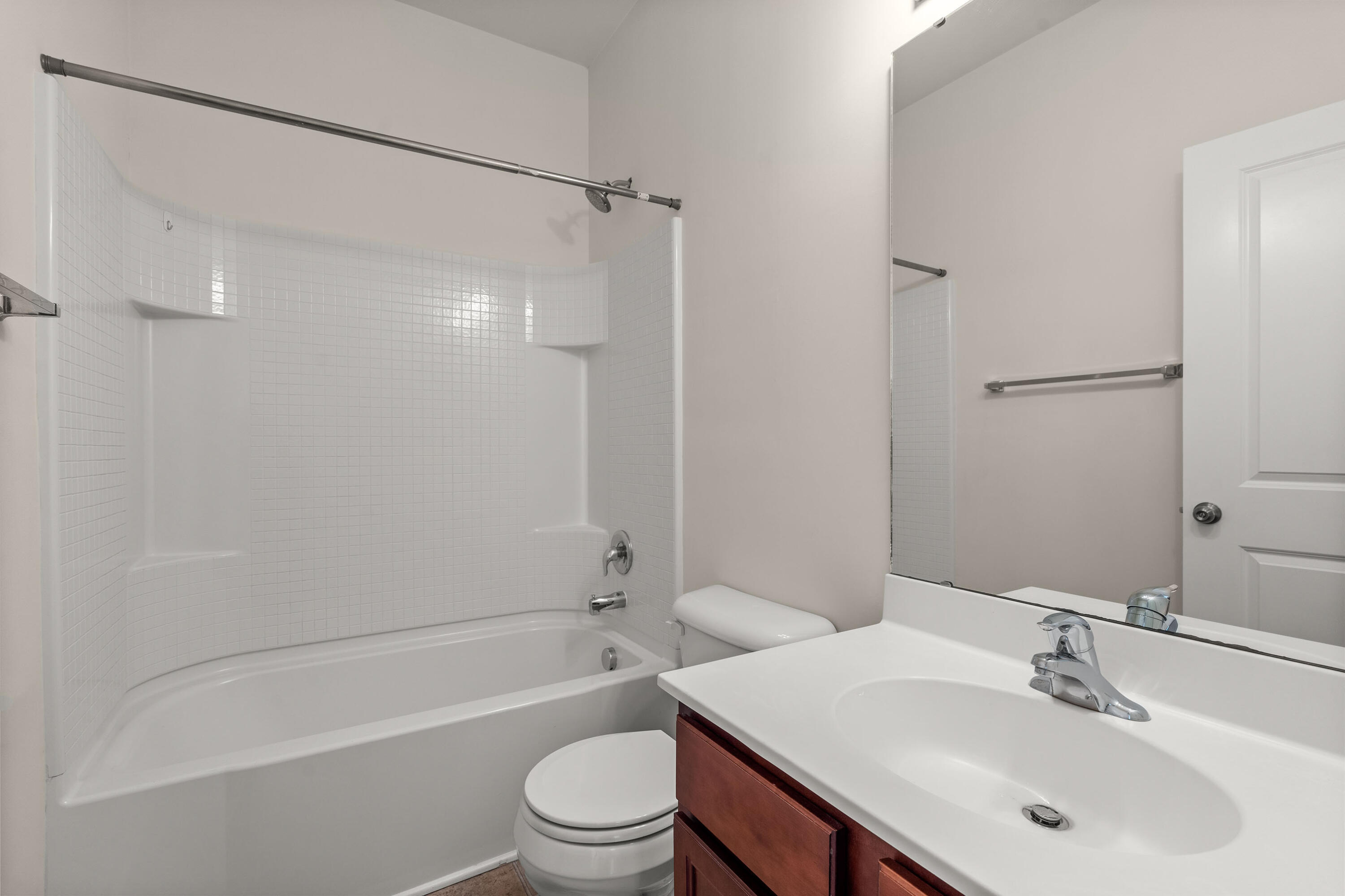 Bathroom with a white tiled tub and shower, toilet, and dark wood vanity.