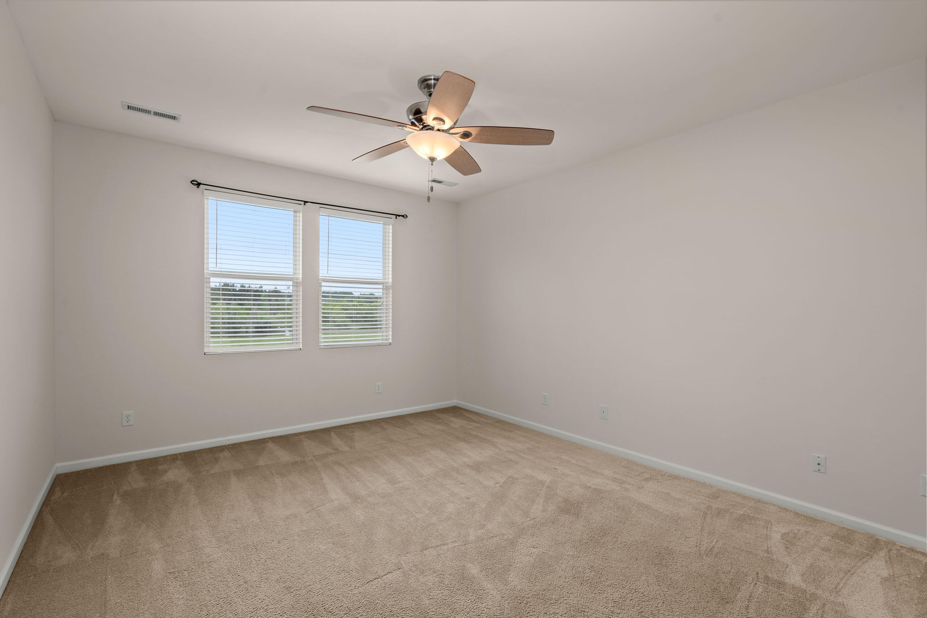 Empty carpeted bedroom with two blinded windows and a ceiling fan with light.
