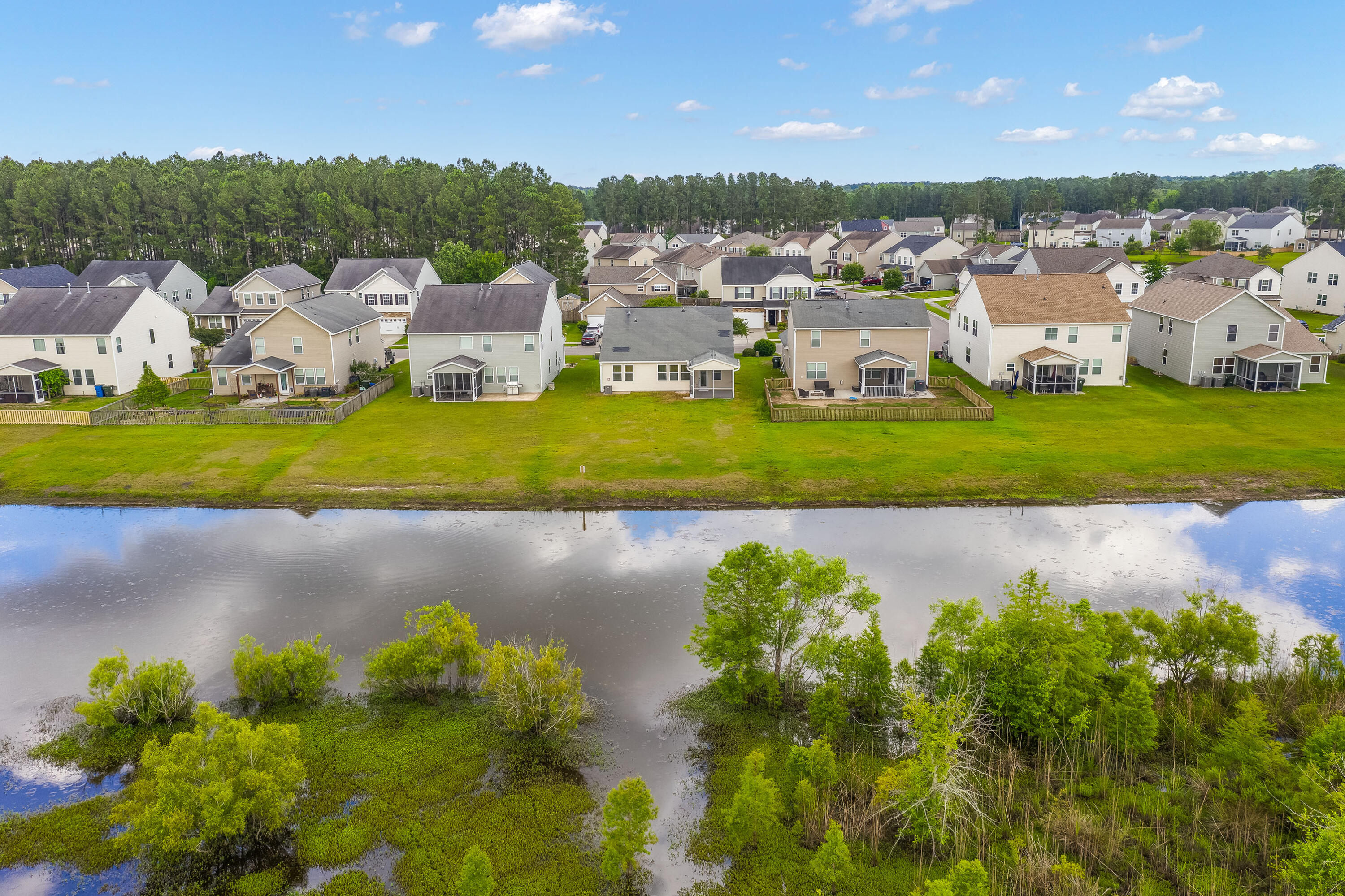 Aerial view of a residential neighborhood across a pond, with wooded wetlands in the foreground.