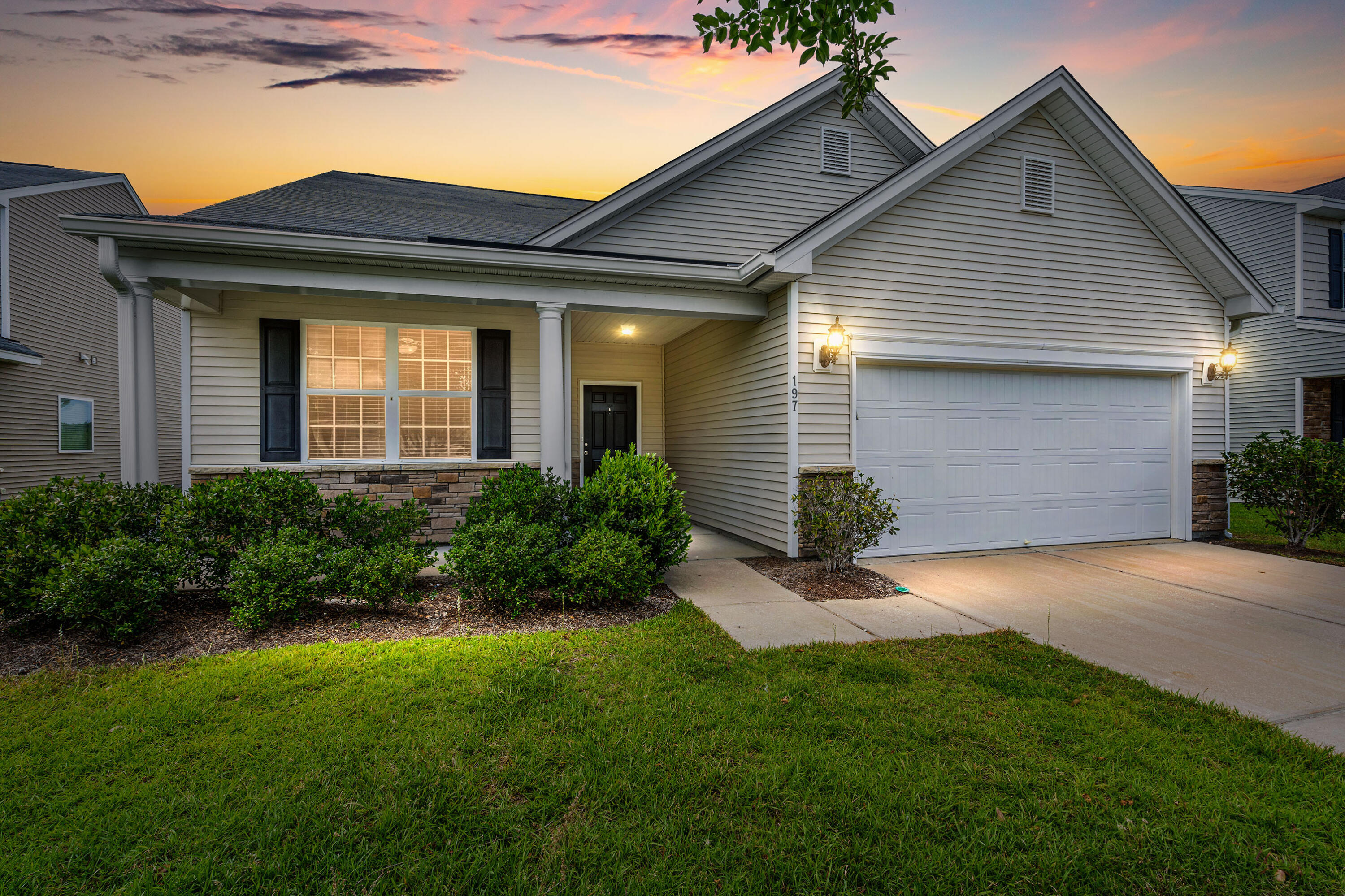 House with a covered porch, stone accents, and two-car garage beneath a colorful dusk sky.