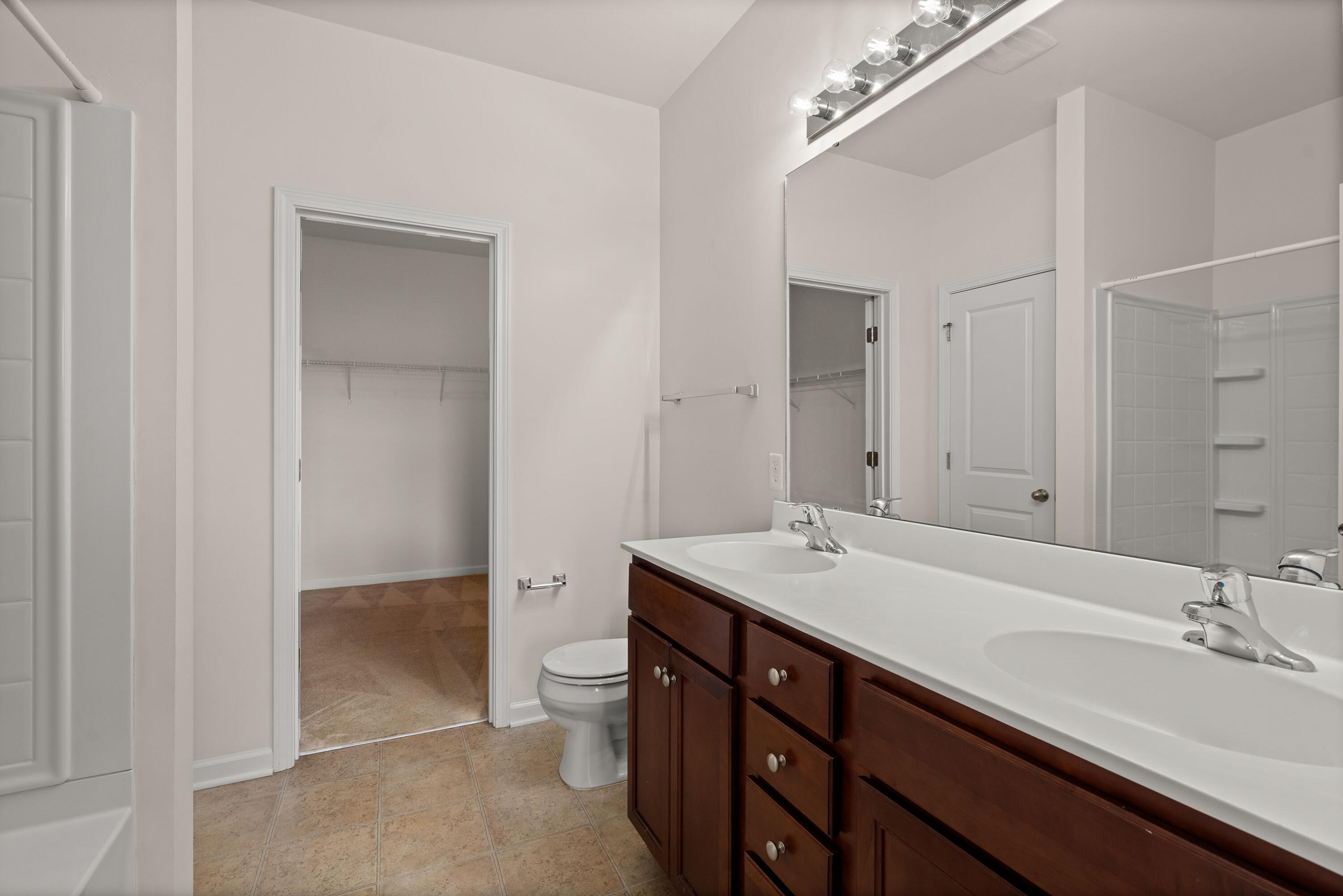Bathroom with a long double vanity, mirrored wall, tiled shower, and open walk-in closet.