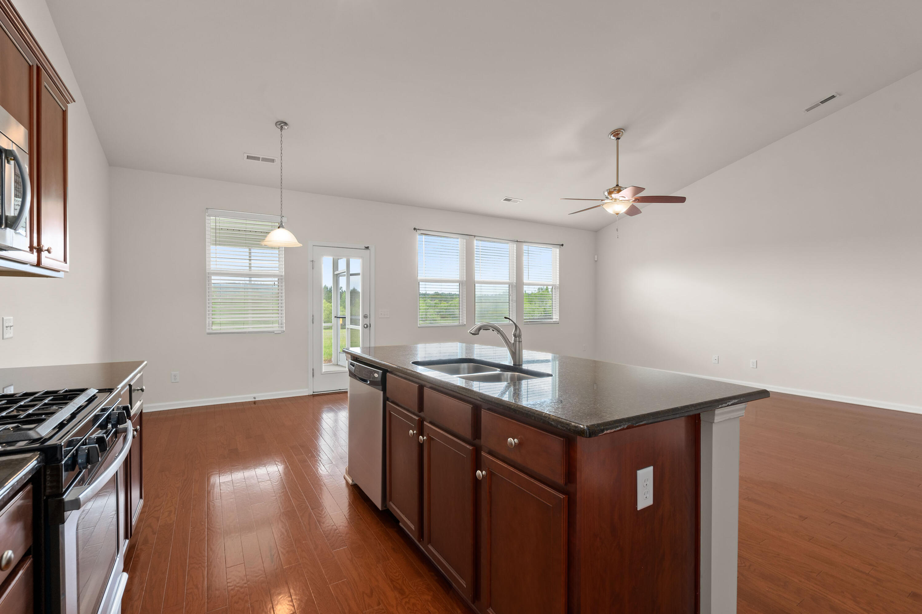 Open kitchen with a large granite island, double sink, dark wood cabinets, and reddish wood flooring.