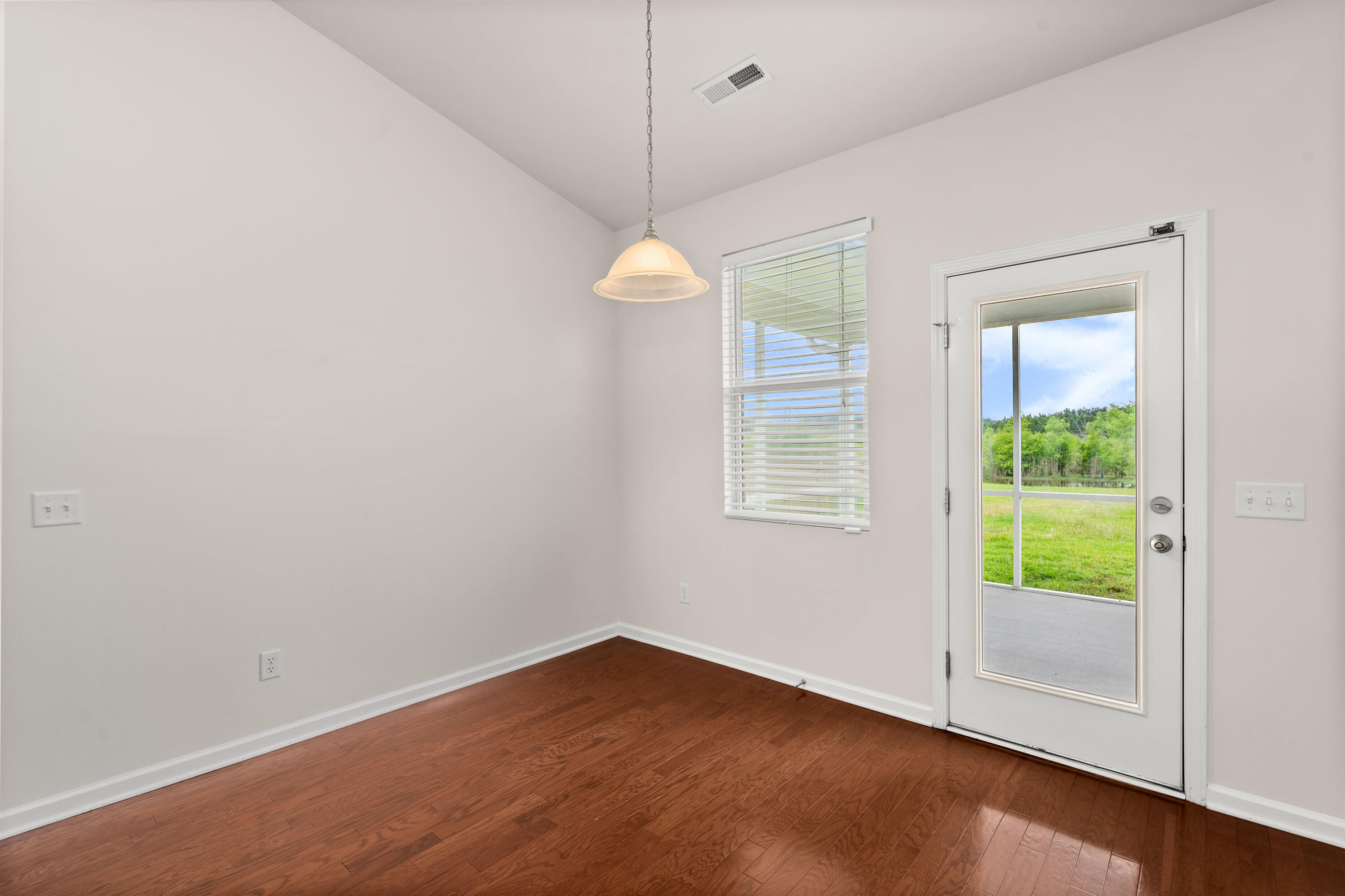 Empty room with hardwood floors, a pendant light, and a glass-panel door to the patio.