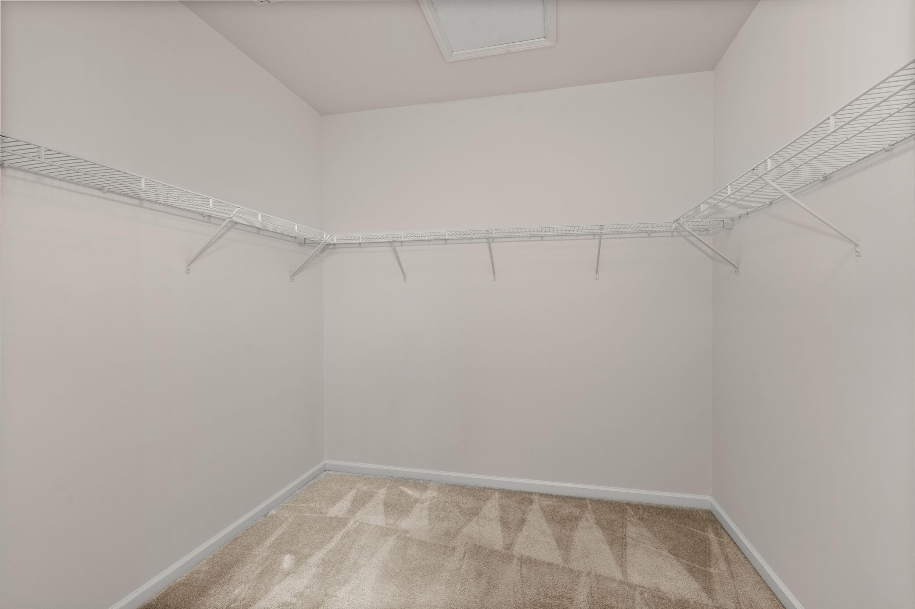 Empty walk-in closet with wire shelving on three walls and beige carpet.