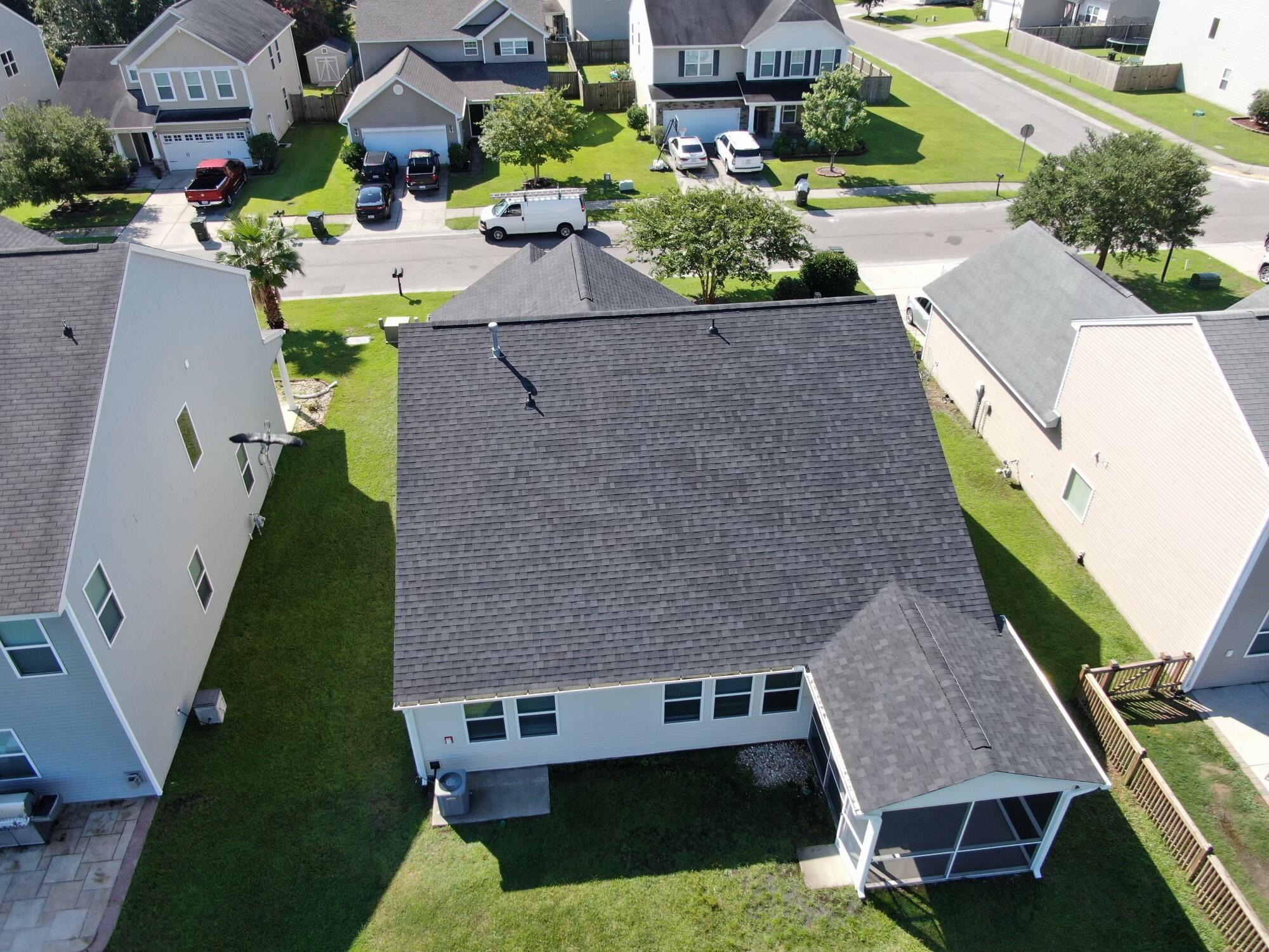 Aerial view of a home’s rear roof, screened porch, and grassy backyard.