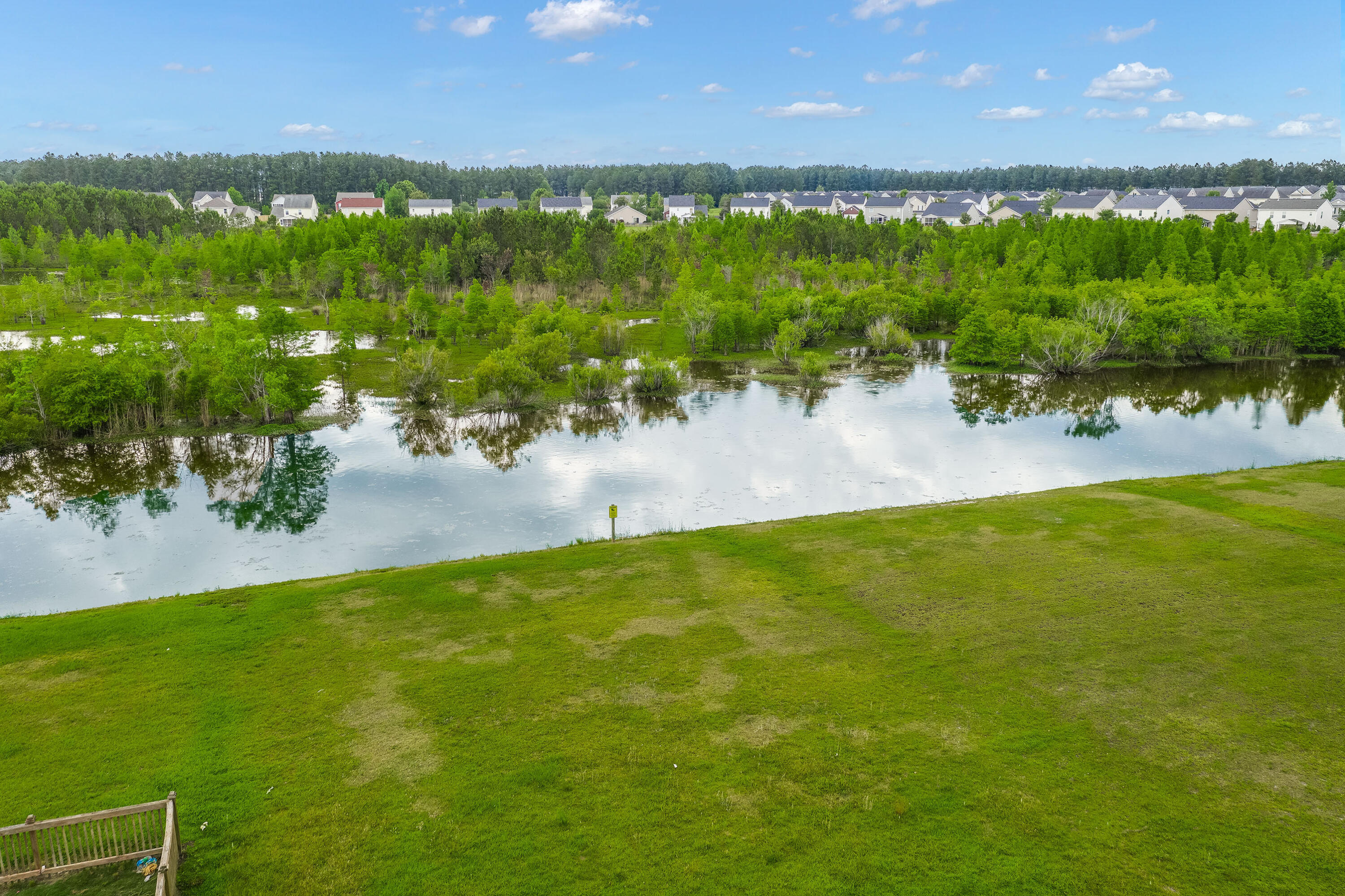 Grassy lawn meets a pond, with wooded wetlands and neighborhood homes in the distance.