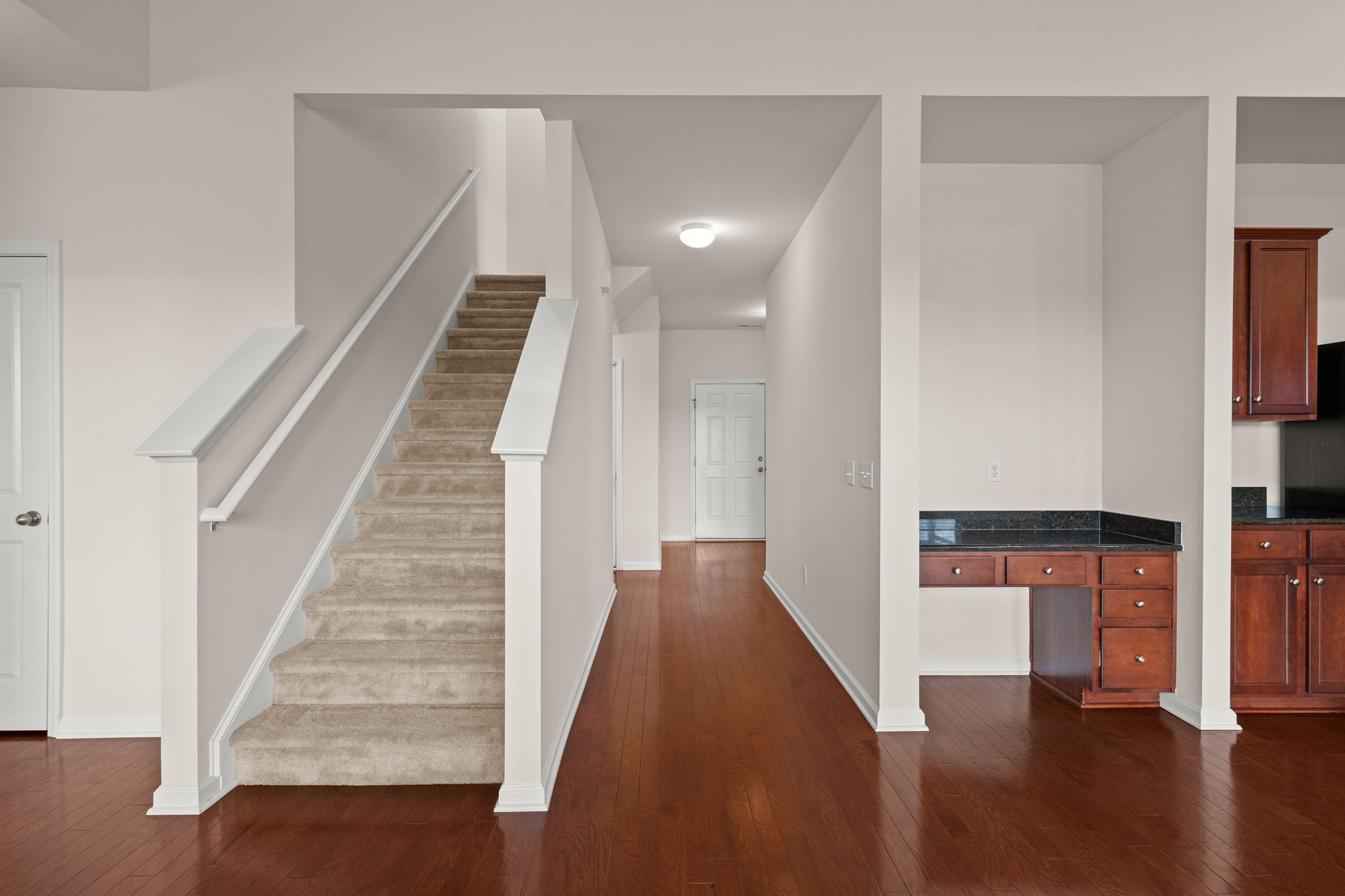 Entryway with carpeted stairs, hardwood floors, a hallway, and dark wood kitchen cabinetry.