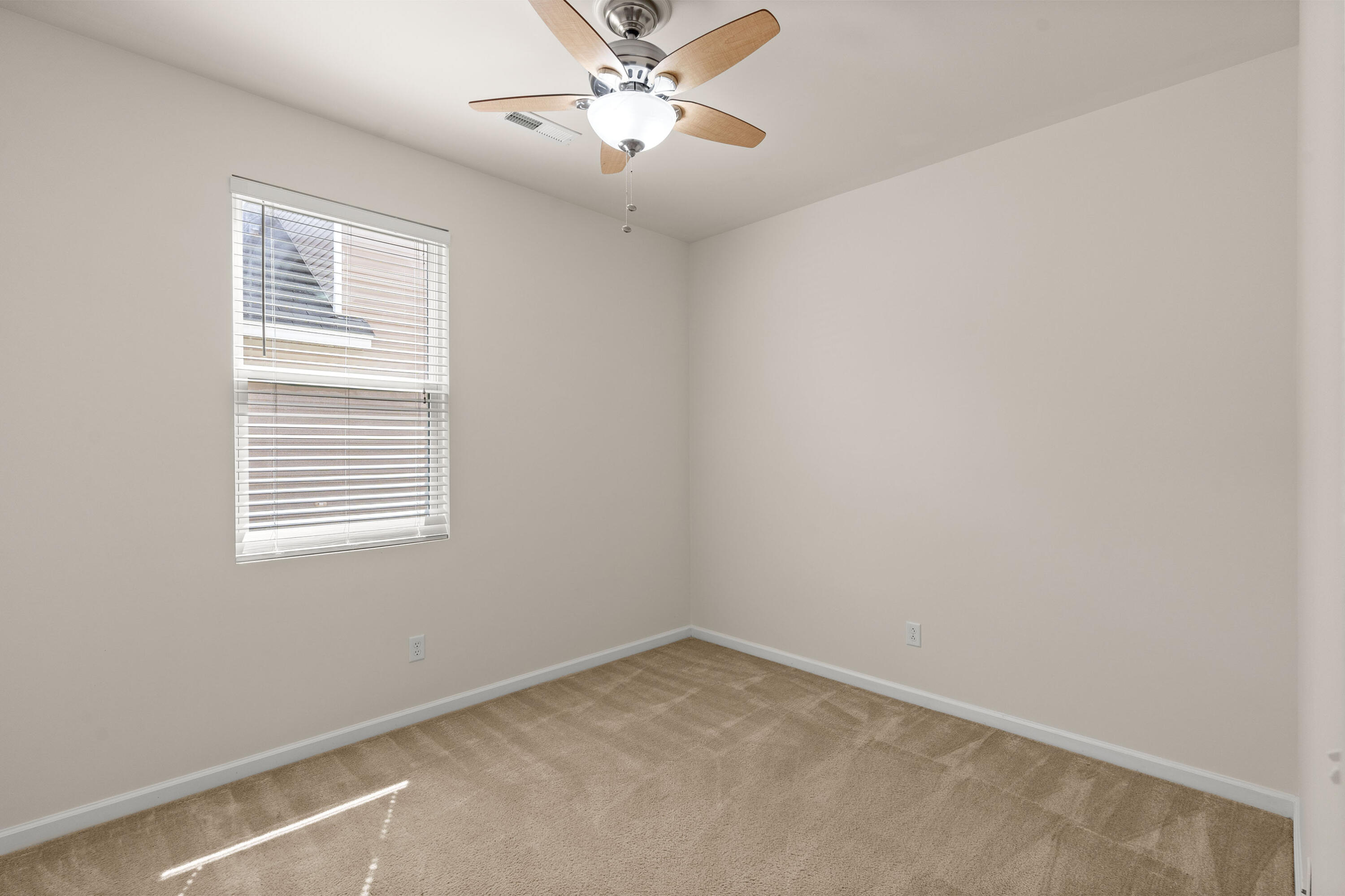 Empty carpeted bedroom with a wood-tone ceiling fan and a window with white blinds.