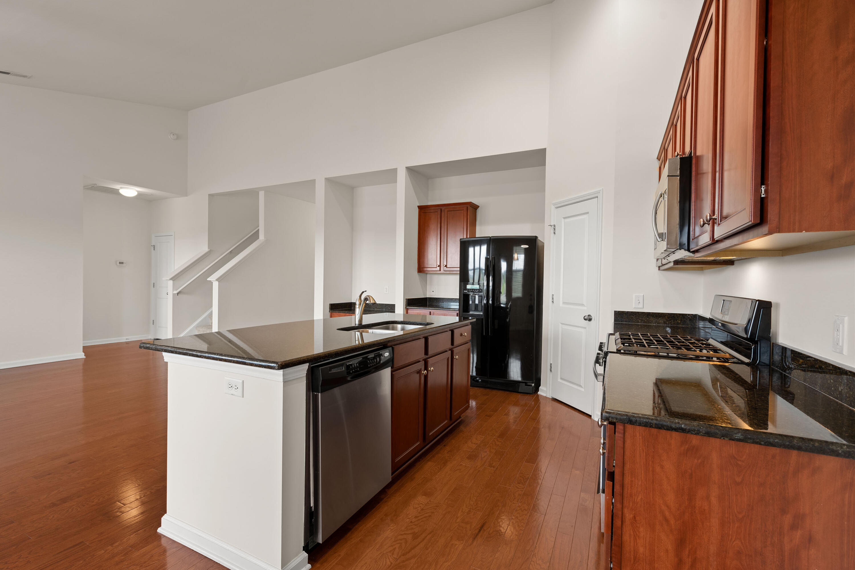 Kitchen with a dark granite island, cherry cabinets, black appliances, and hardwood floors.