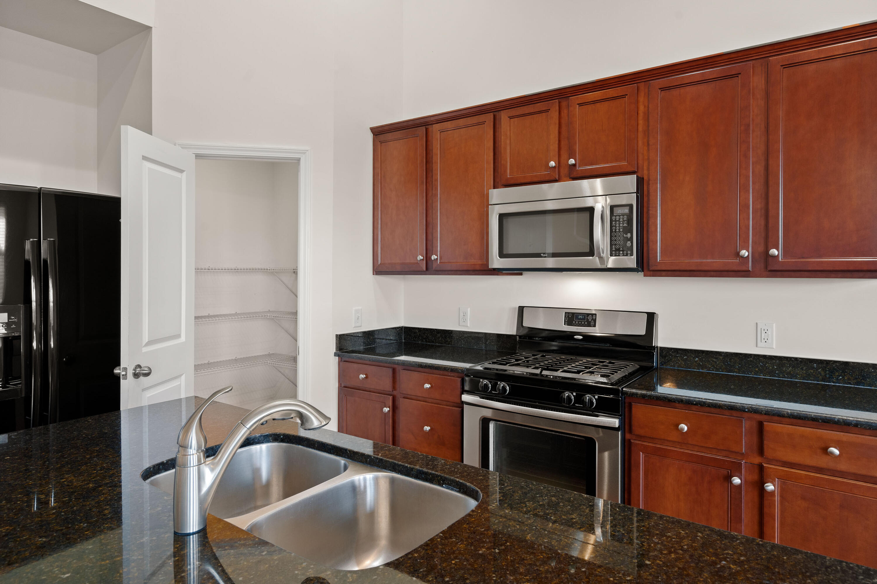 Kitchen with wood cabinets, dark granite counters, stainless steel appliances, and a double-basin sink.