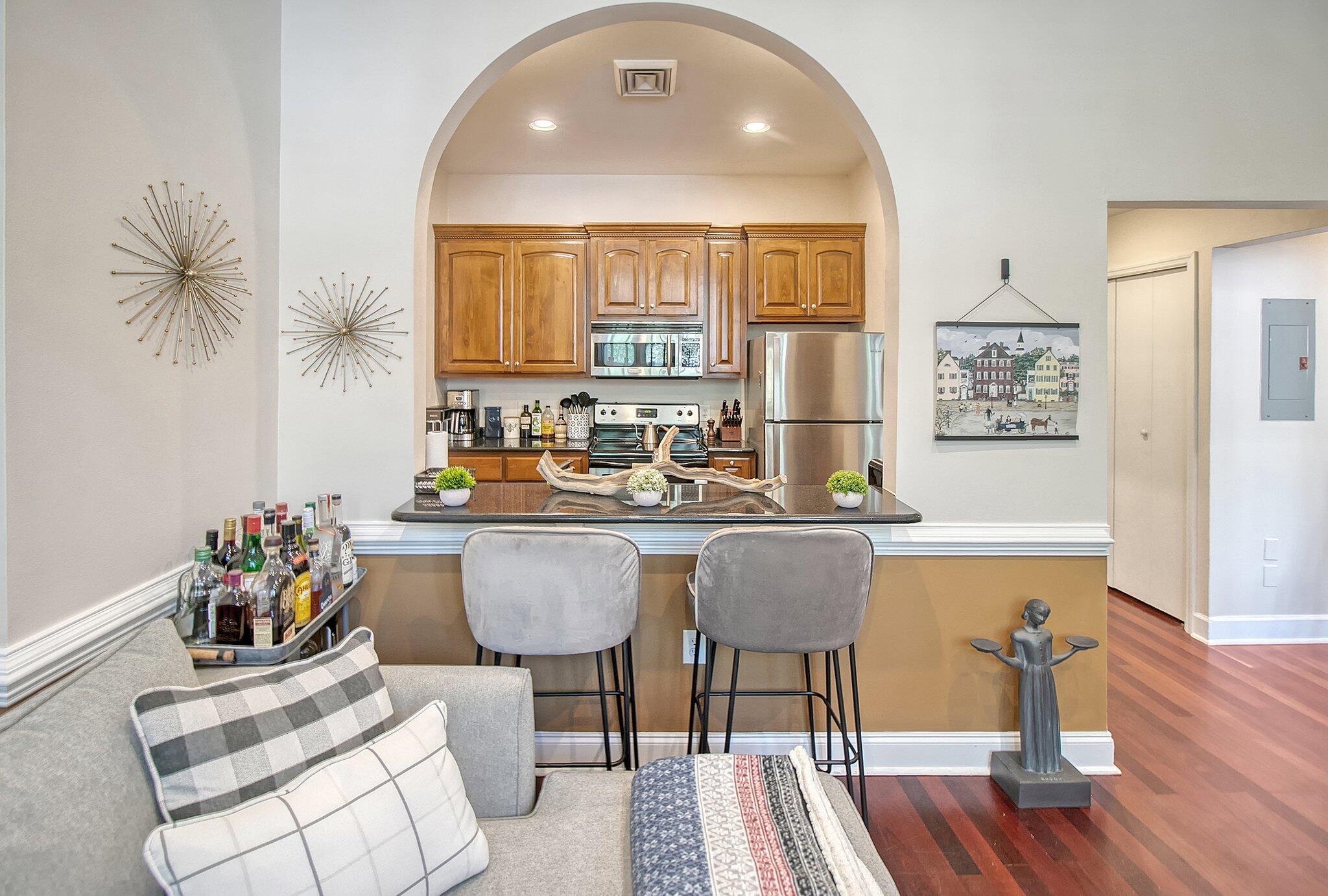 Kitchen with arched wood cabinetry, stainless appliances, and a granite breakfast bar beside the living area.