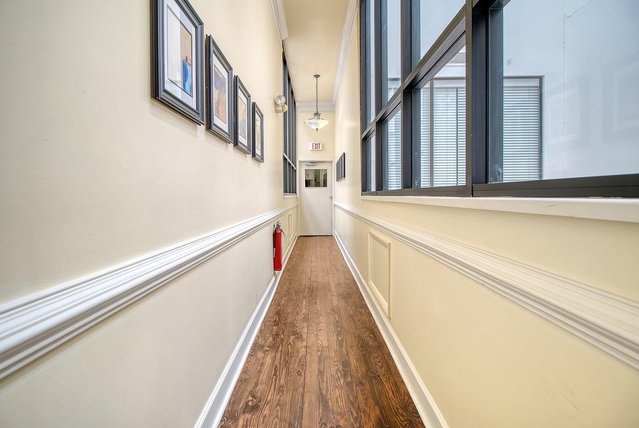 Interior hallway with wood plank flooring, framed artwork, and large windows along one side.