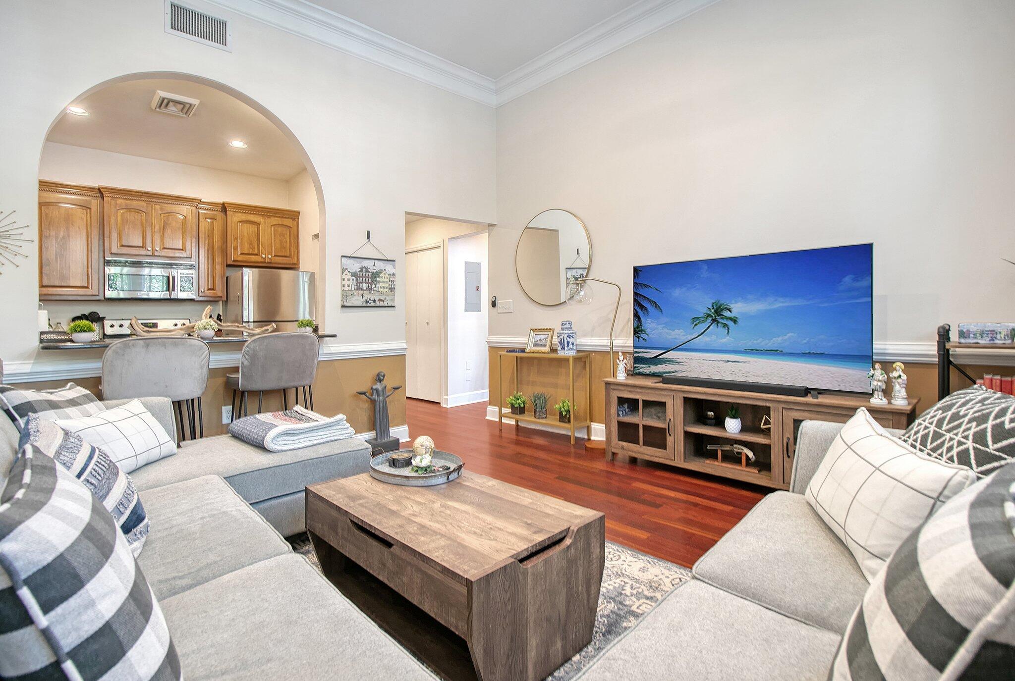 Living room with gray sectional sofas, a large television, hardwood floors, and an arched opening to the kitchen.