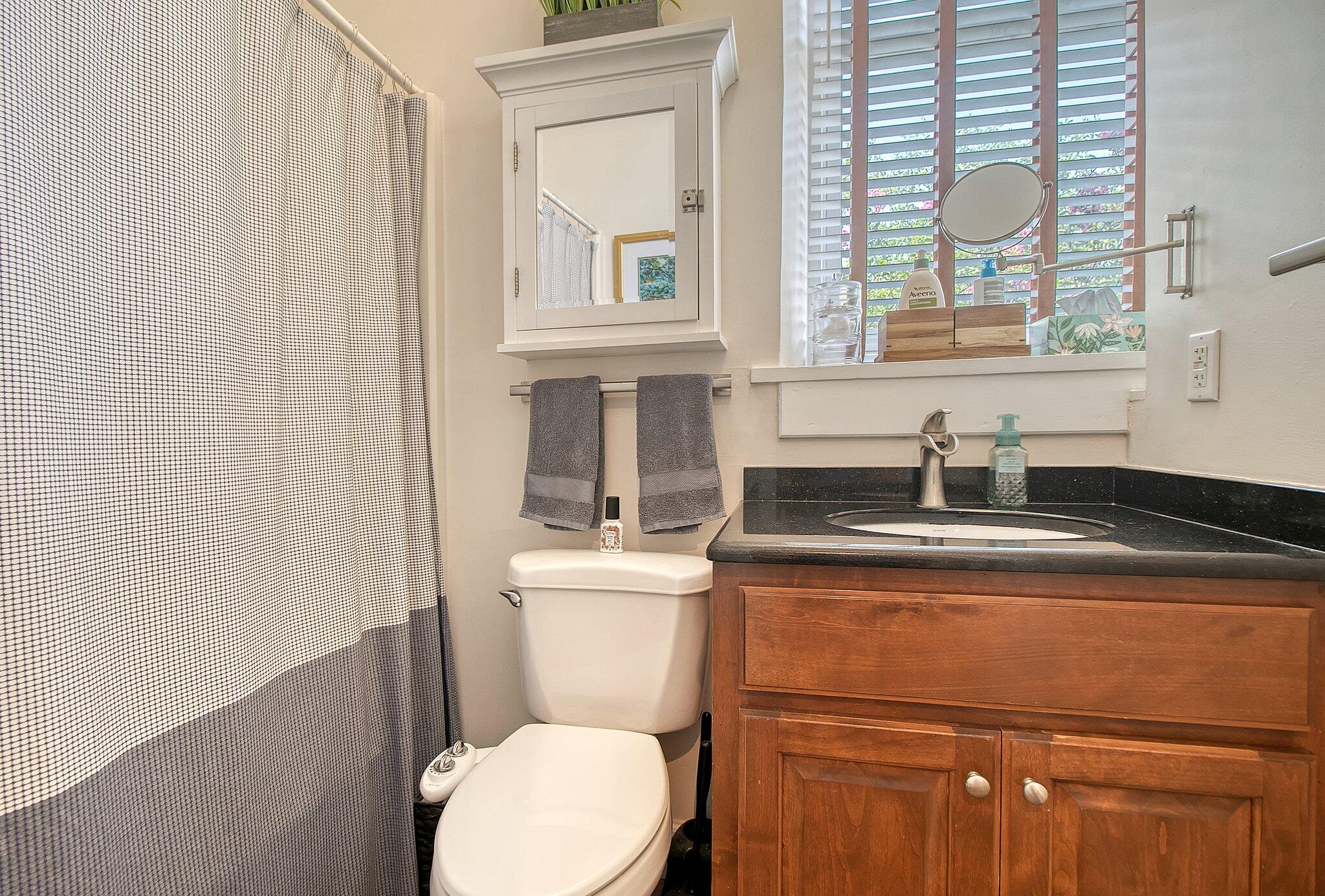 Bathroom with a wood vanity, black countertop, and plantation shutters above the sink.